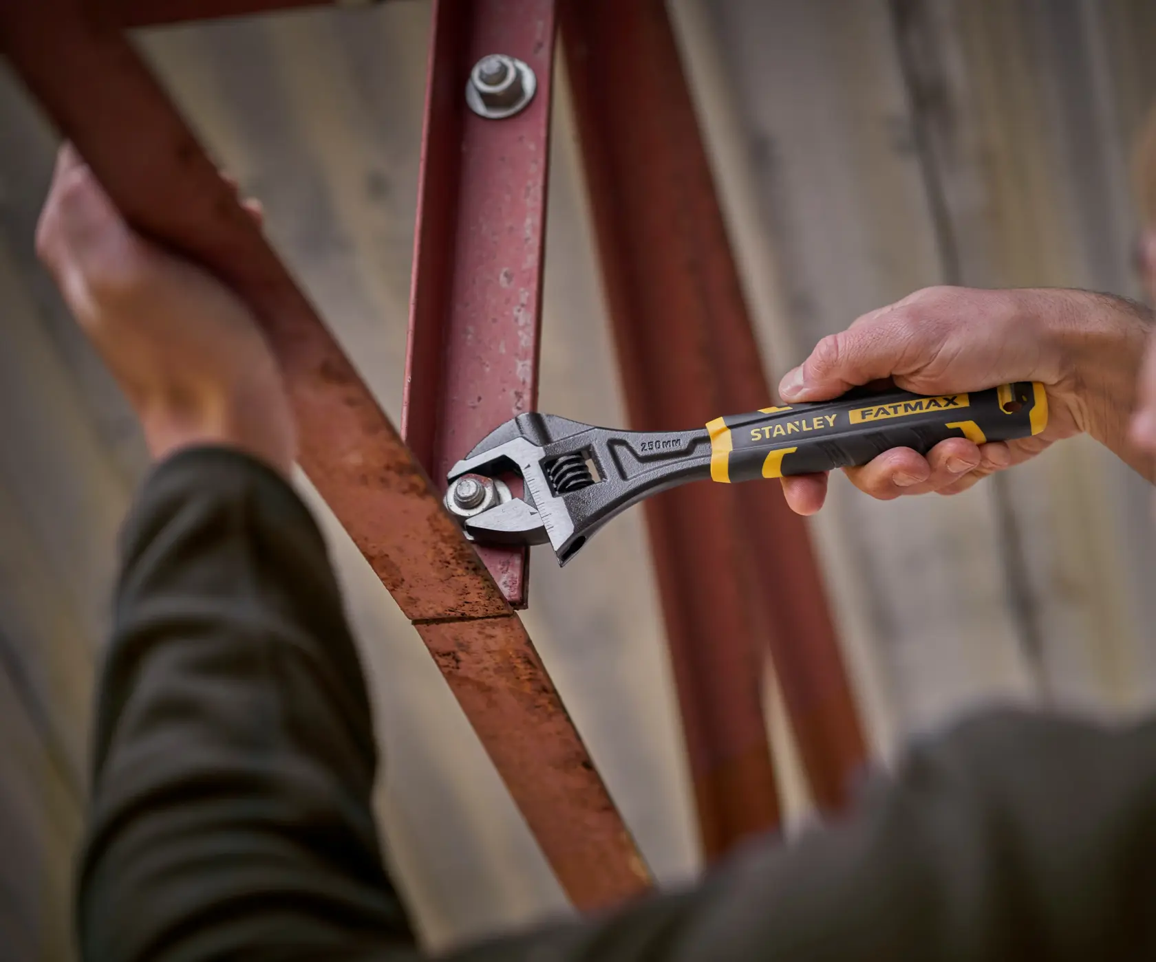 Stanley FMHT13127-0 adjustable wrench used to tighten bolt on red metal beam, close-up action shot.