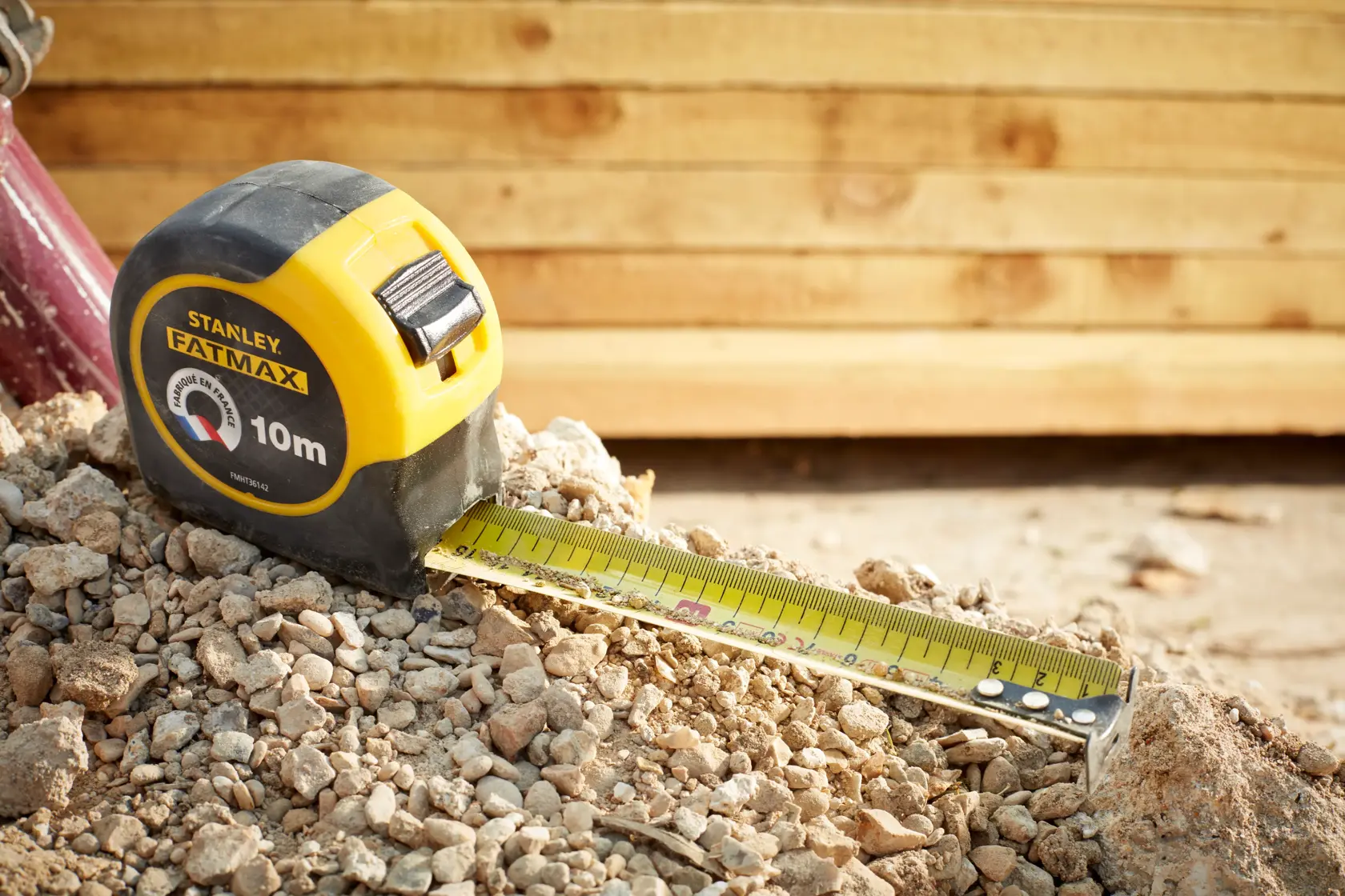 Foto des STANLEY FMHT36142-0 FATMAX 10m Maßbands auf steinigem Boden mit gelbem Holz im Hintergrund.