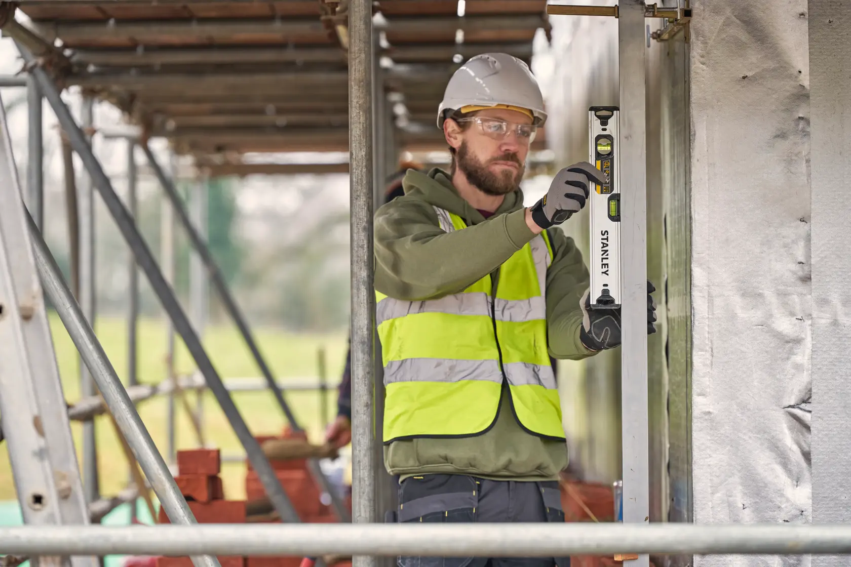 Foto eines Arbeiters mit STANLEY FMHT43671-1 Wasserwaage auf Baustelle, trägt Warnweste und Helm.