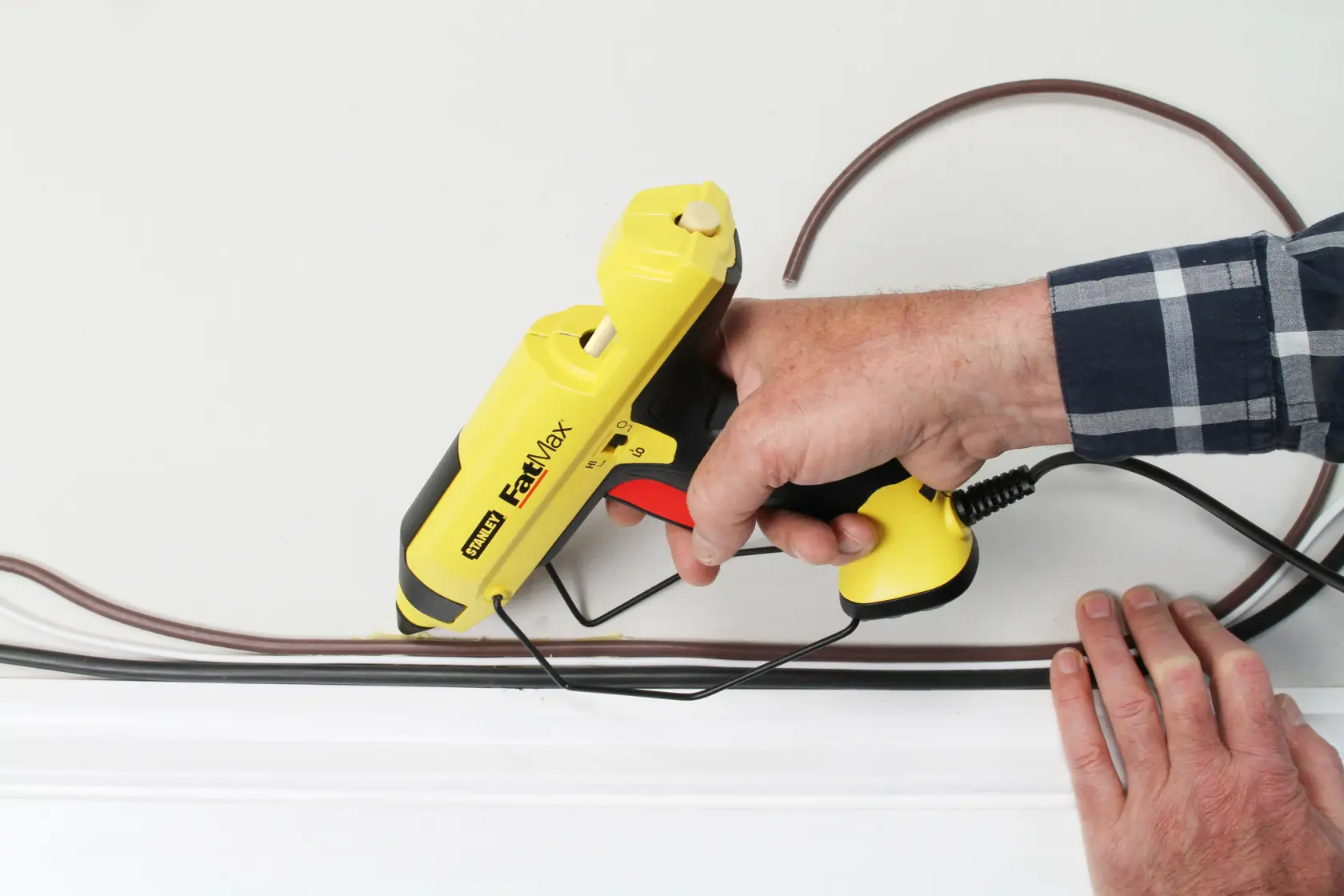 Yellow and black Stanley FatMax hot glue gun with stand and power cord, shown on a white background.