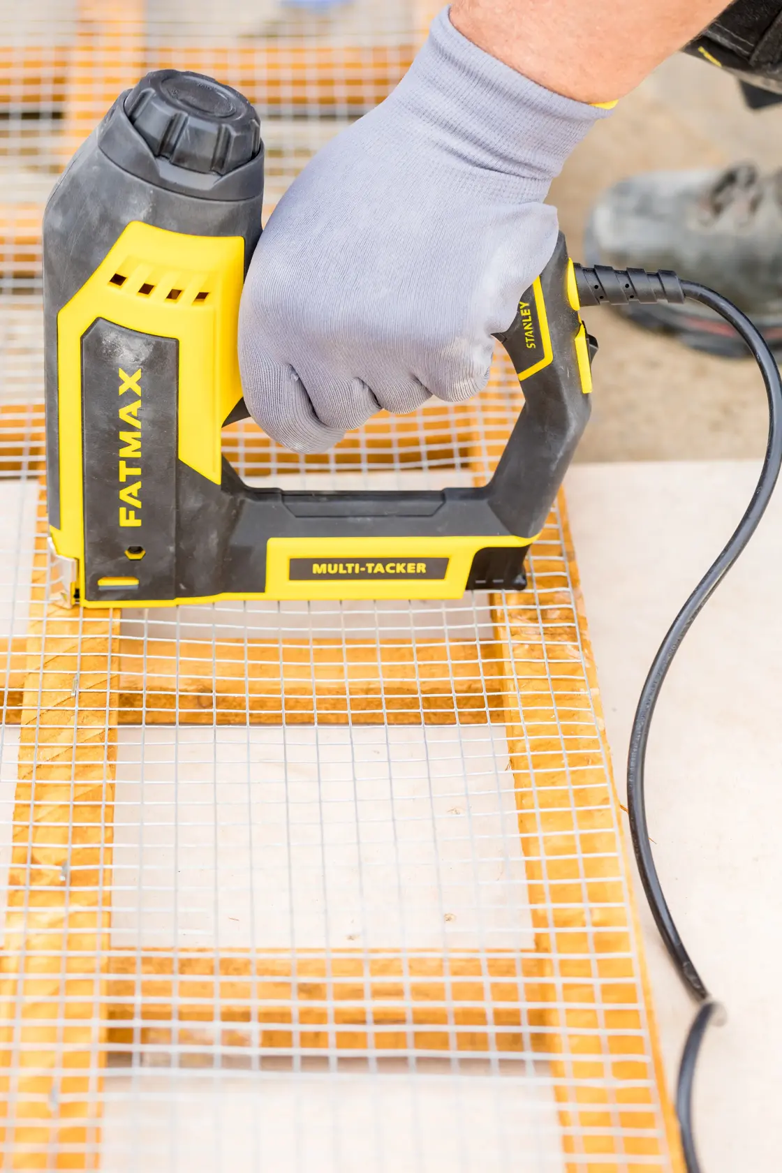 Foto des STANLEY FATMAX FMHT6-75934 Elektro-Multitackers, der Drahtgitter auf Holz befestigt, Nahaufnahme im Einsatz.