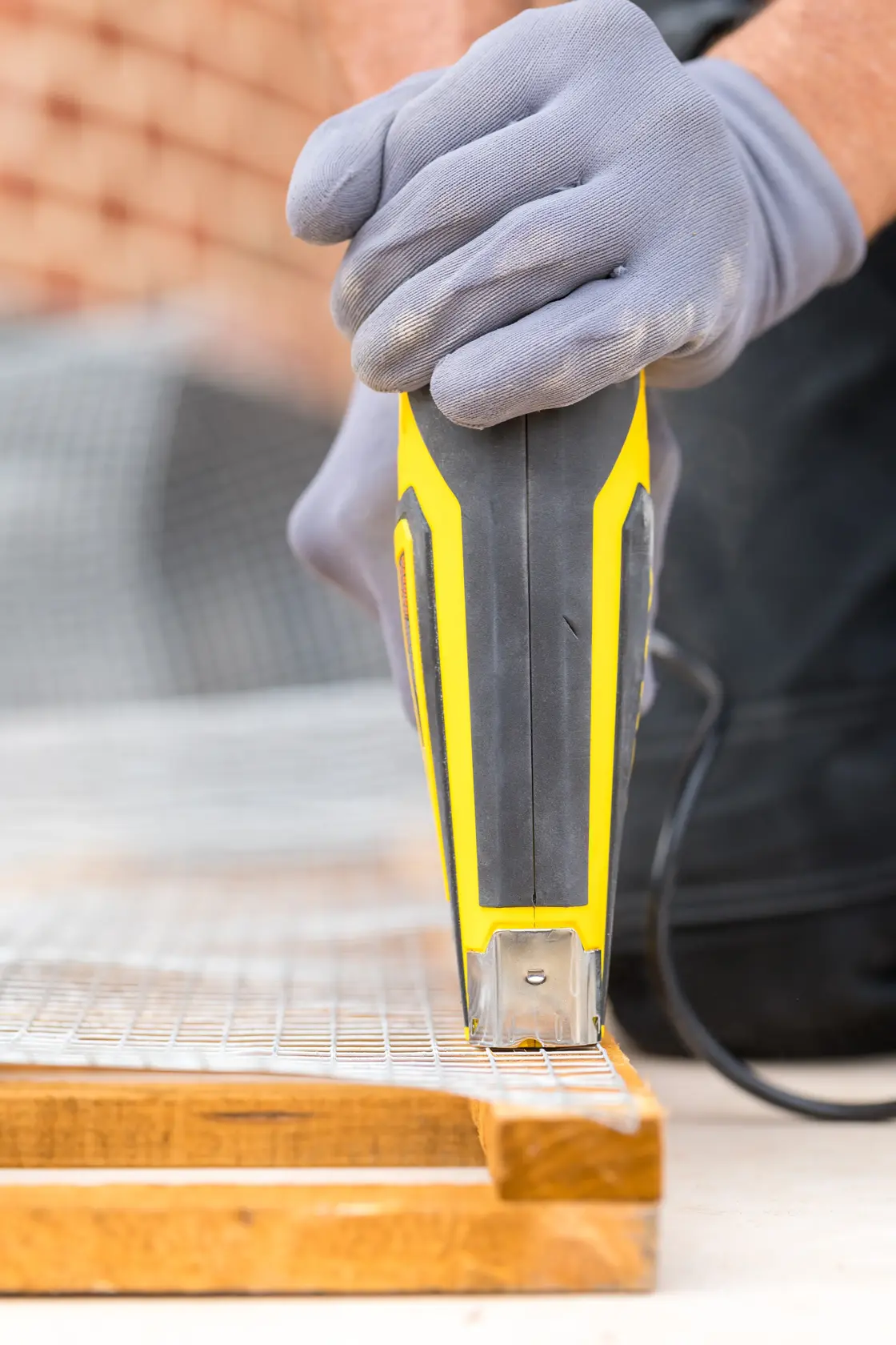 STANLEY FMHT6-75934 Elektrotacker Nahaufnahme auf Drahtgeflecht und Holz, behandschuhte Hand bedient das Gerät.