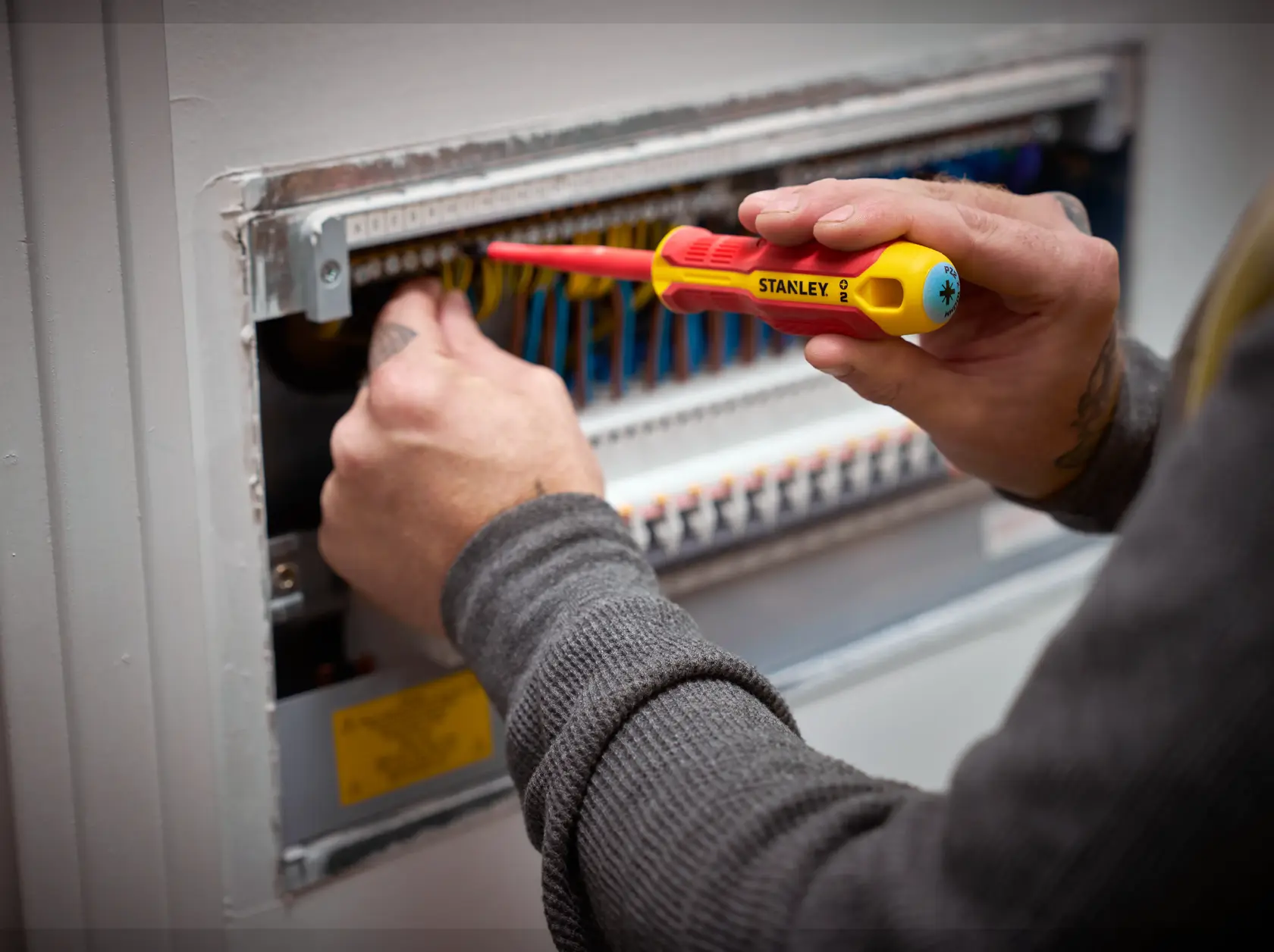 Person arbeitet mit einem STANLEY isolierten Schraubendreher an einem elektrischen Panel mit bunten Kabeln.