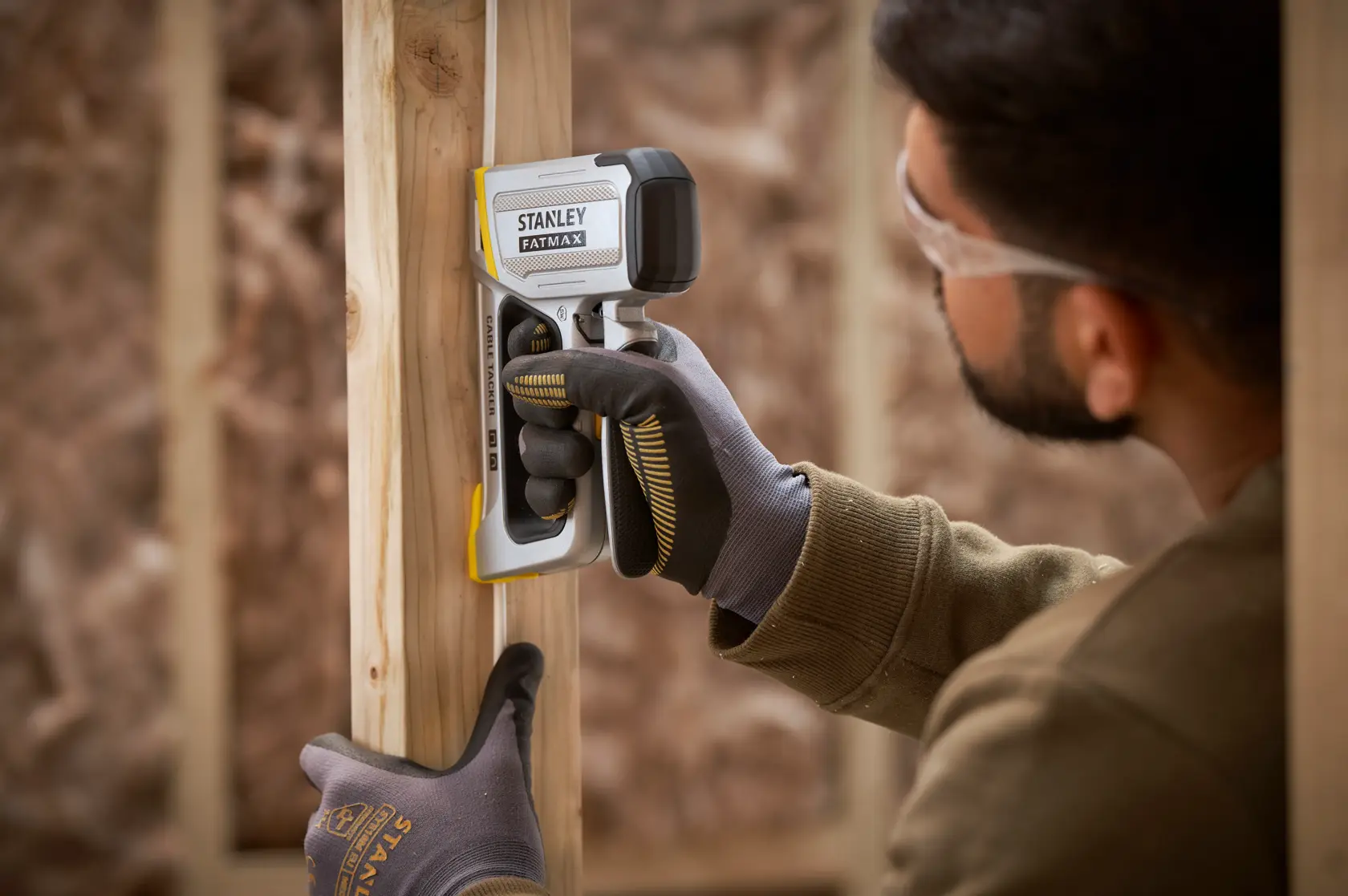 STANLEY FMHT70100-0 stud finder held by gloved hand against wooden frame in construction setting.