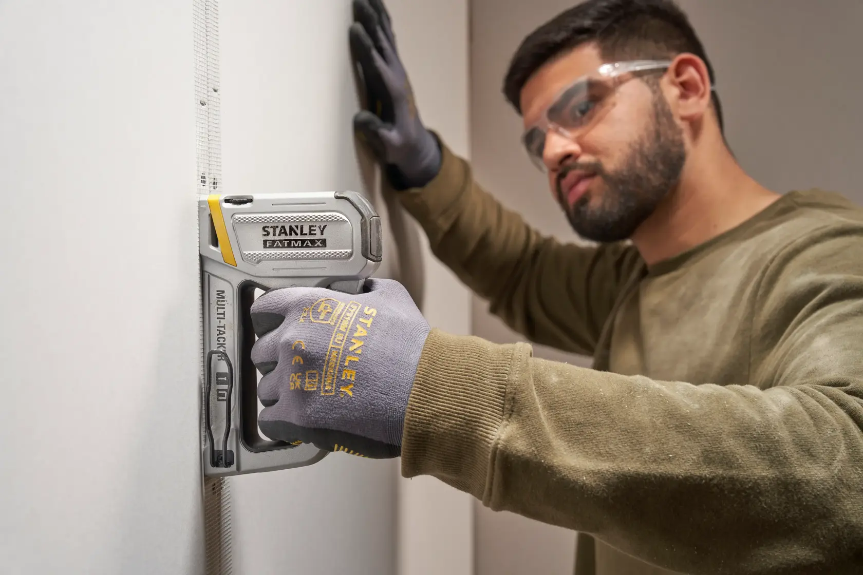 Foto einer Person, die mit einem STANLEY FMHT70250-0 Tacker auf Gipskarton arbeitet und STANLEY Handschuhe trägt.