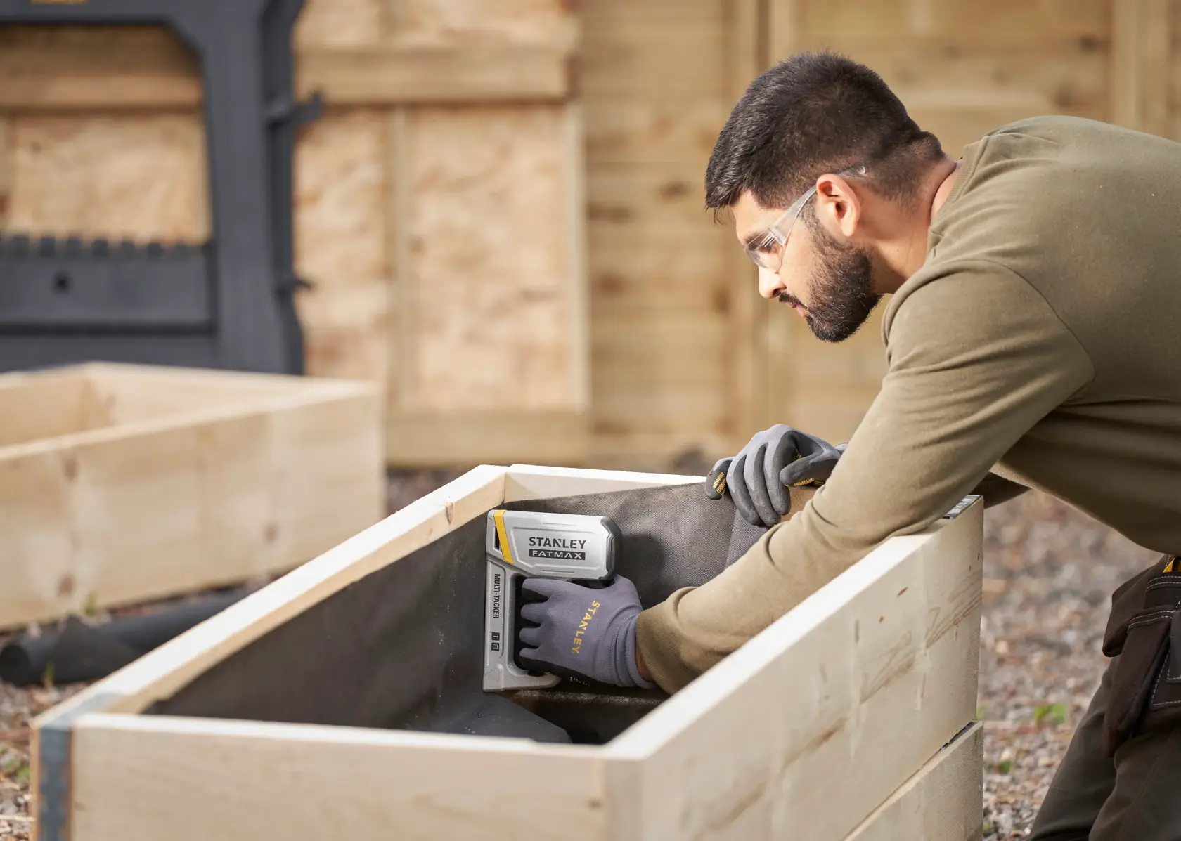 Stanley FMHT70443-0 stapler in use for woodworking, person wearing Stanley gloves outdoors.