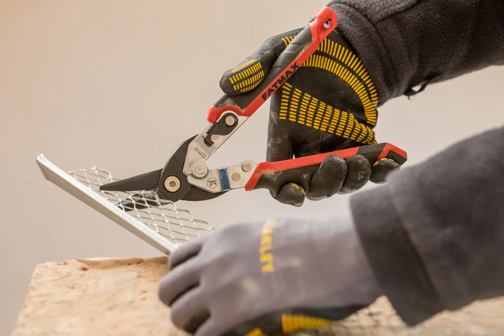 STANLEY FMHT73755 Metallschere schneidet Gitter, Nahaufnahme, Handschuhe in Schwarz und Gelb.