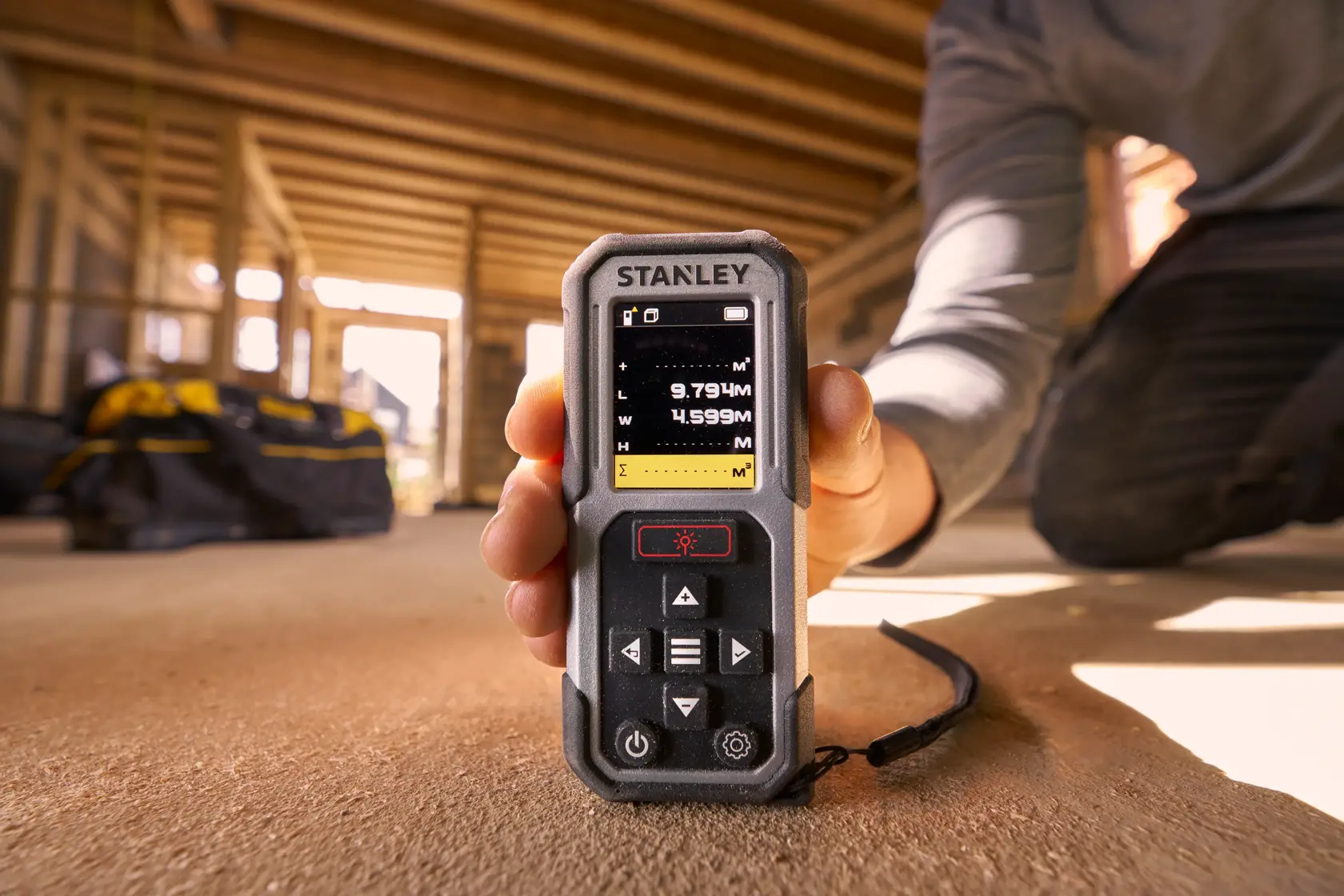 Foto des STANLEY FMHT77050-XJ Laser-Entfernungsmessers, gehalten auf einer Baustelle, Display sichtbar.