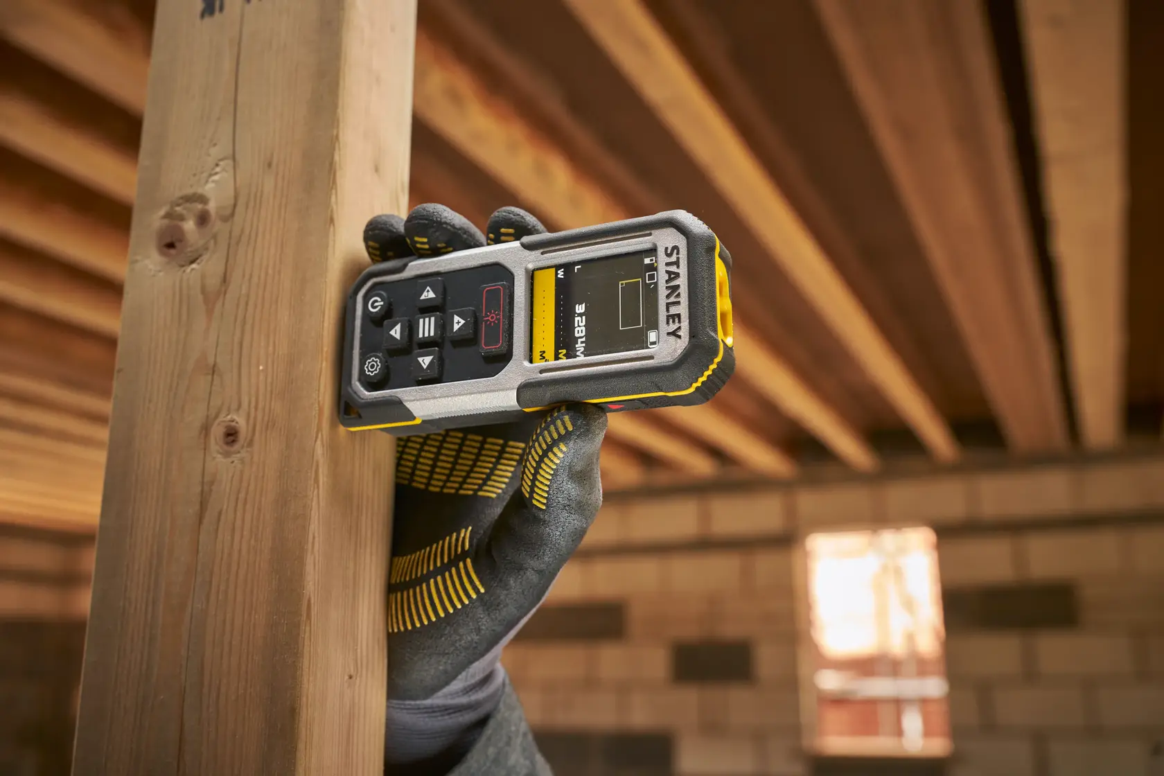 Foto des STANLEY FMHT77050-XJ Laser-Entfernungsmessers im Einsatz, Display und Tasten sichtbar, in behandschuhter Hand gehalten.