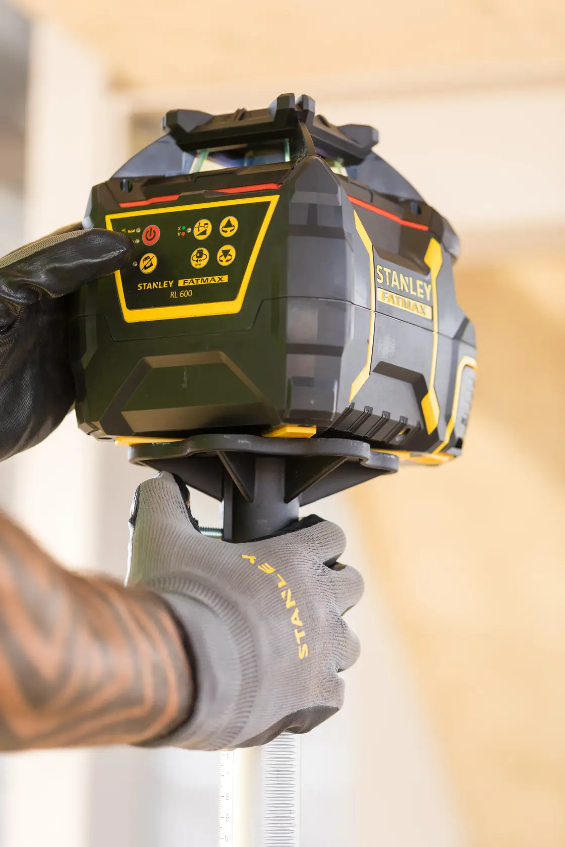 Foto des STANLEY FMHT77446-1 Rotationslasers, bedient von einer behandschuhten Hand auf einer Baustelle.