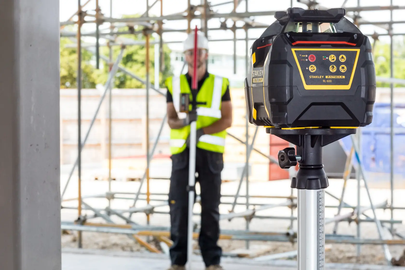 STANLEY FMHT77446-1 Rotationslaser auf Stativ auf Baustelle, Arbeiter im Hintergrund.