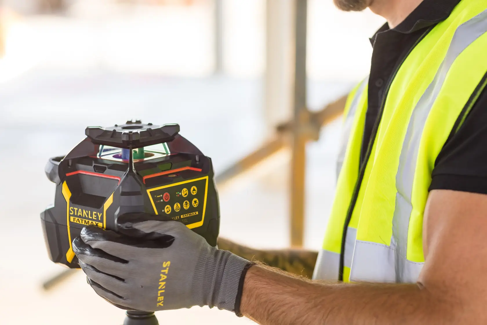 Foto des STANLEY FMHT77447-1 Laser-Nivelliergeräts, gehalten von Arbeiter mit Sicherheitsweste und Handschuhen.