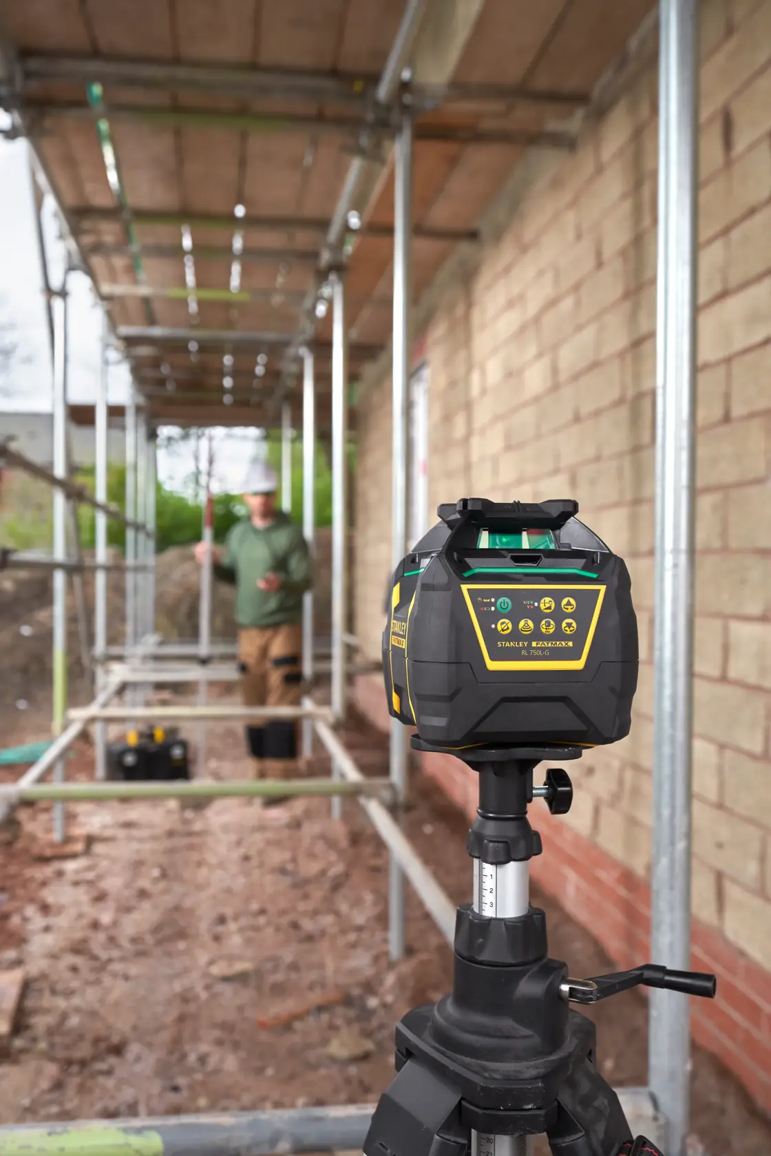 STANLEY FMHT77448 Rotationslaser auf Stativ an Baustelle, Fokus auf dem Gerät mit Arbeiter im Hintergrund.