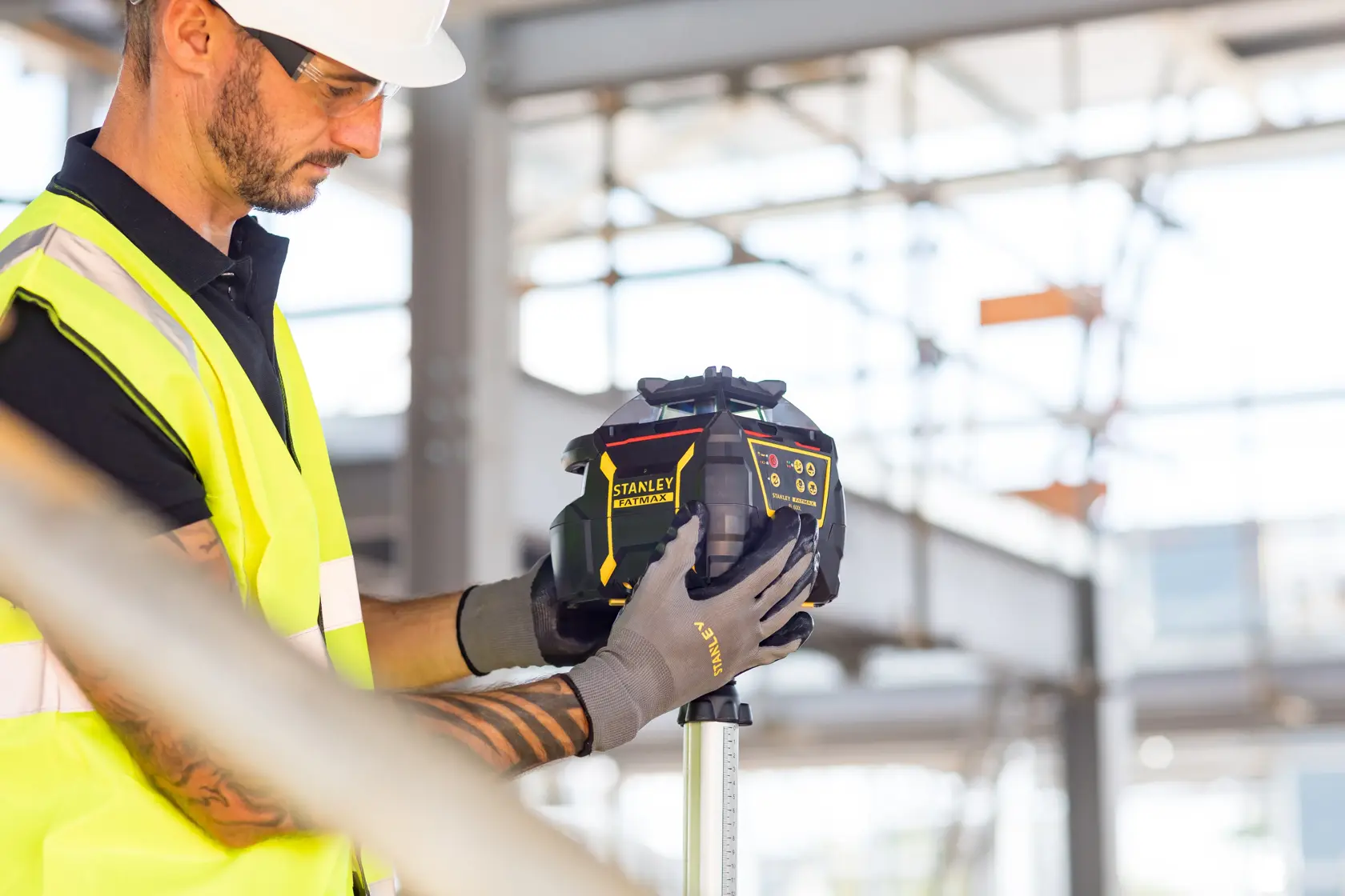 STANLEY FMHT77449-1 Laser-Nivelliergerät von Arbeiter im Warnweste auf Baustelle gehalten.