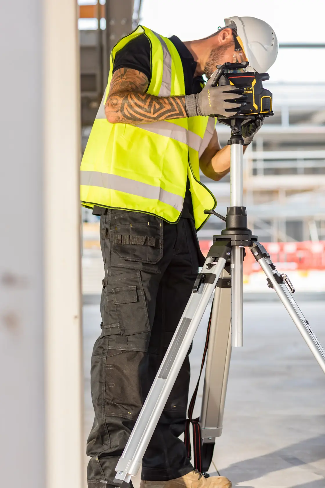 STANLEY FMHT77449-1 Bau-Laser-Nivelliergerät auf Stativ, verwendet von Arbeiter mit Weste und Helm.