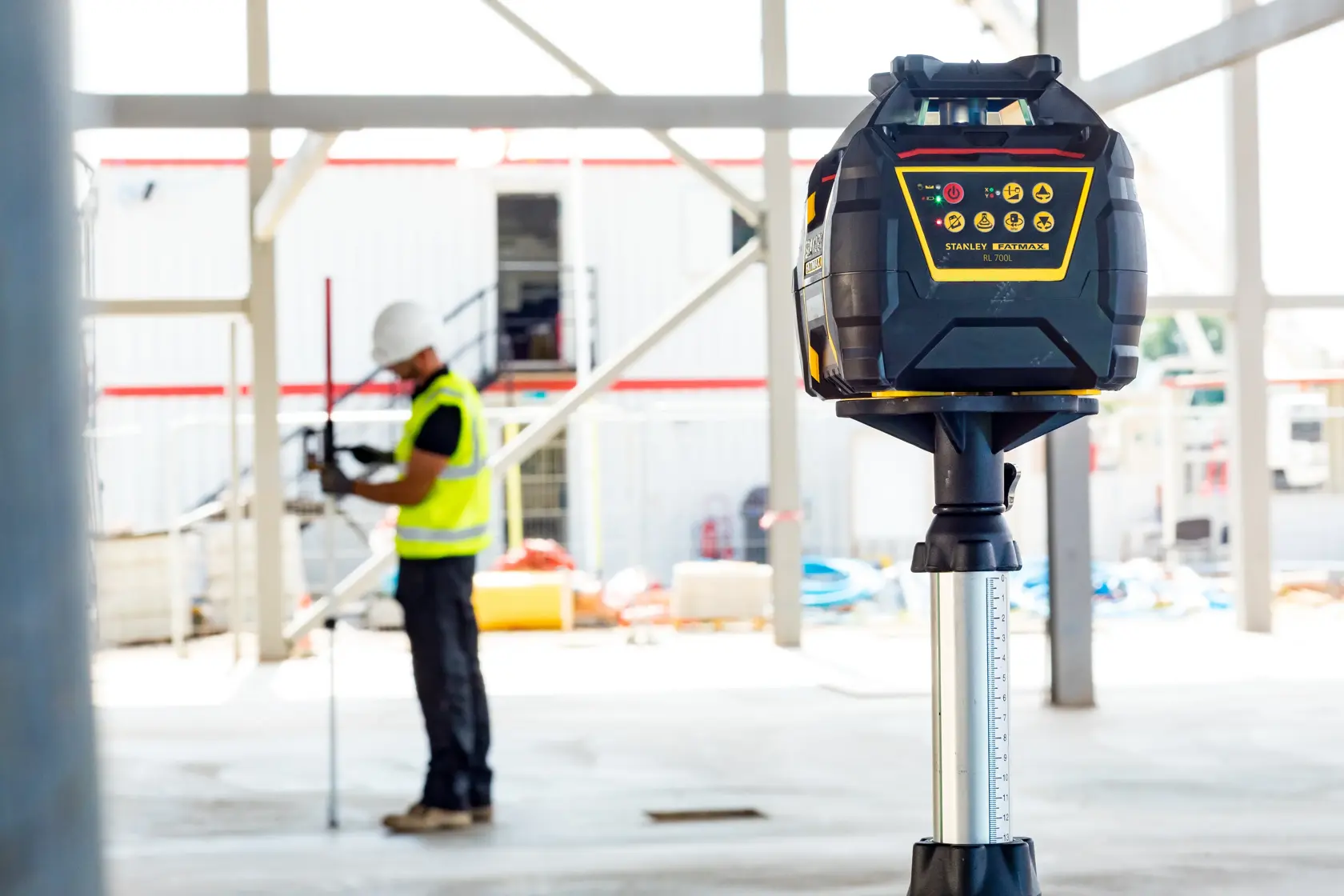STANLEY FMHT77449-1 Rotationslaserniveau auf Stativ an Baustelle, Arbeiter im Hintergrund.