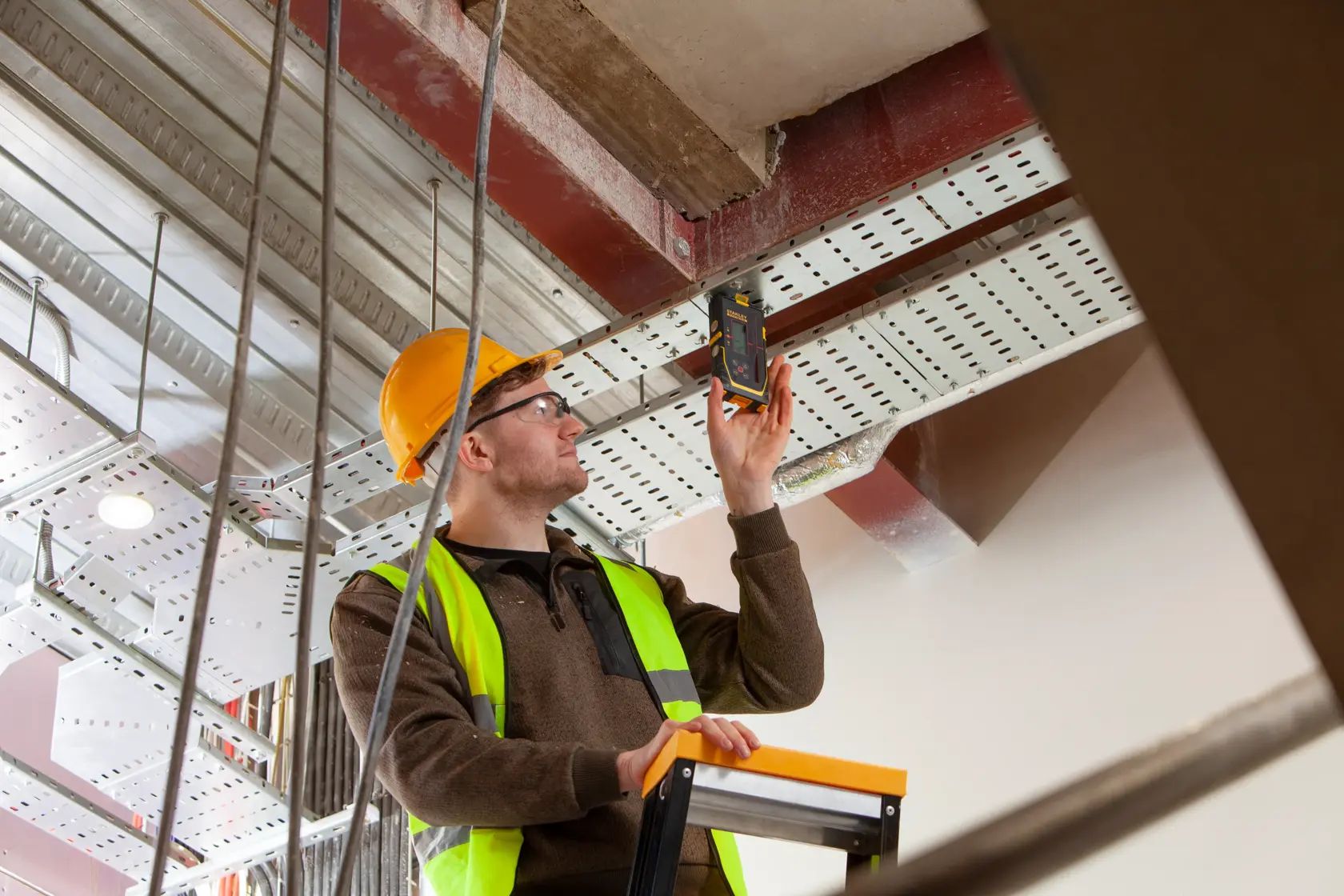 Fotografie des digitalen Detektors STANLEY FMHT77652-0, verwendet von Arbeiter mit Sicherheitsausrüstung auf Baustelle.