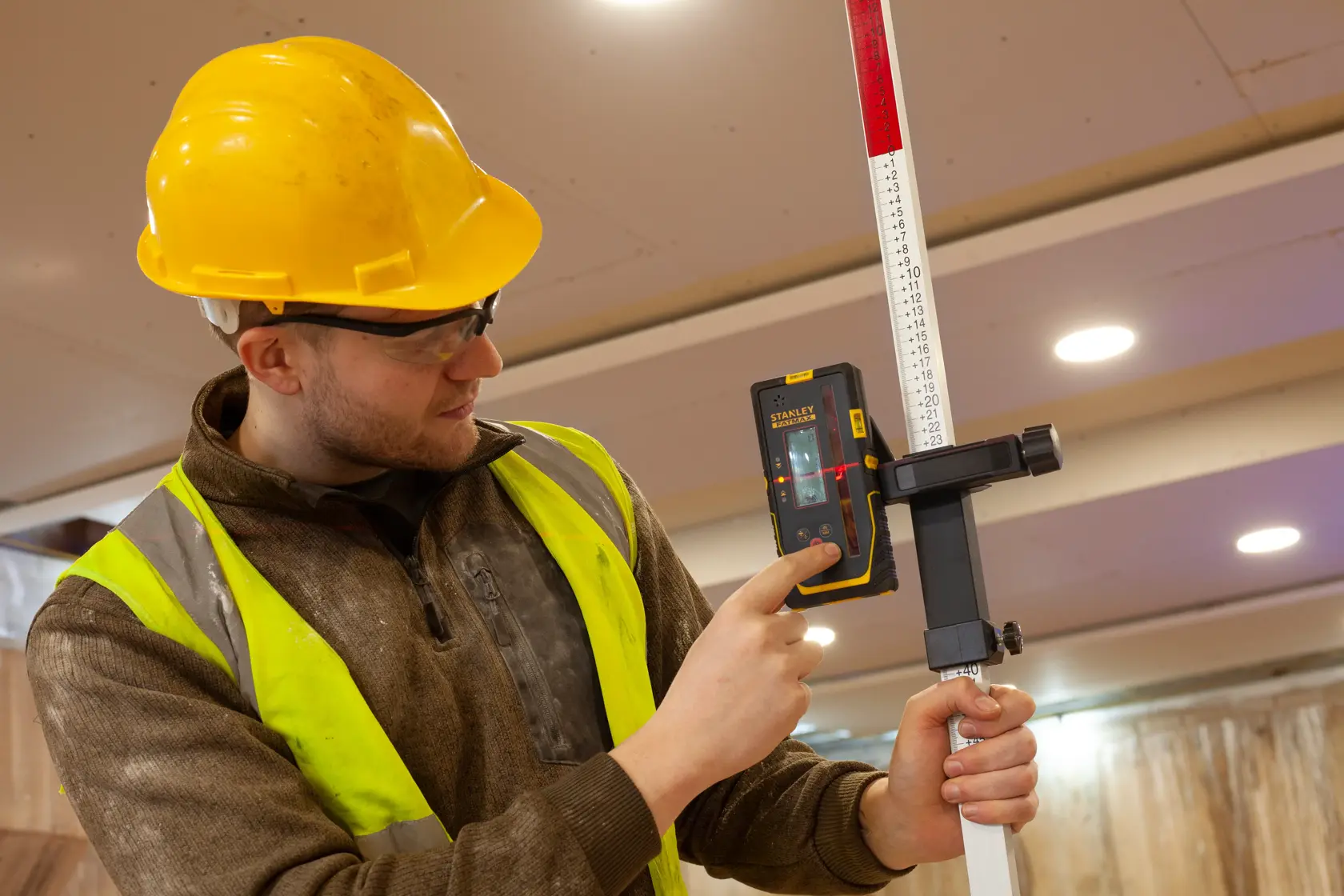 STANLEY FMHT77652-0 Laser-Empfänger, von Arbeiter gehalten und an Messstab befestigt.
