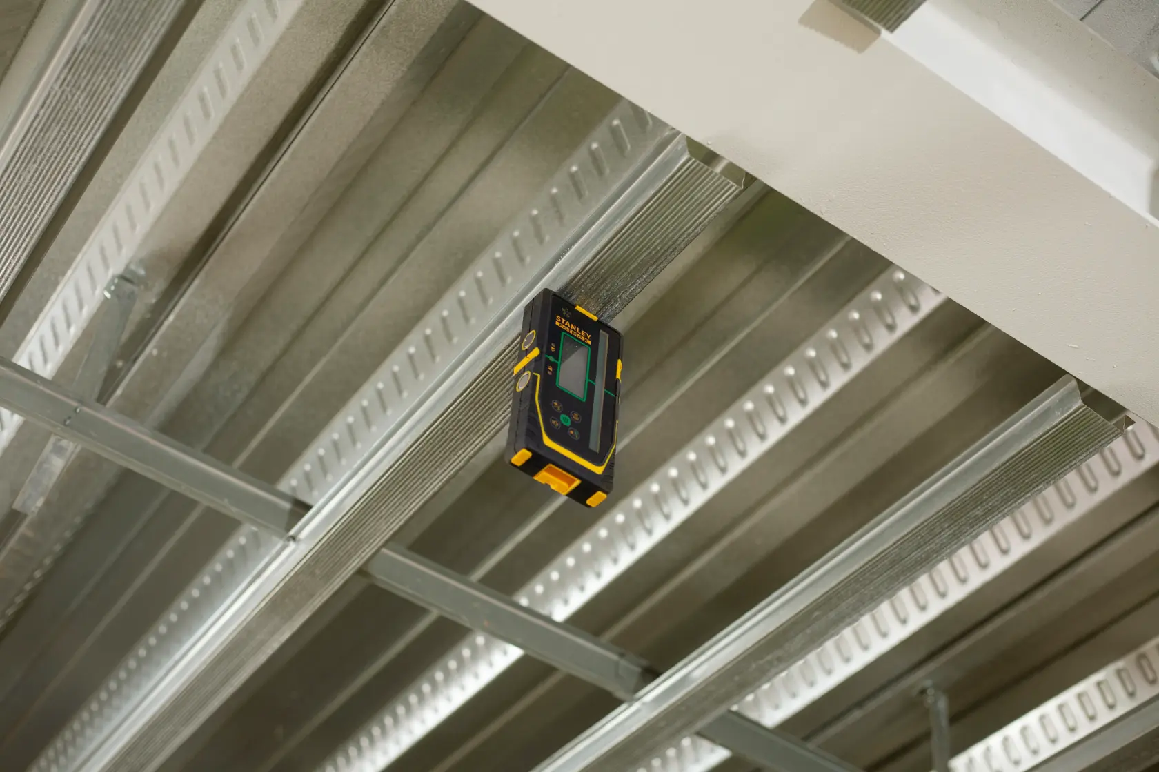 Foto des STANLEY FMHT77653-0 Laser-Detektors an Metall-Deckenkonstruktion, Frontanzeige sichtbar.