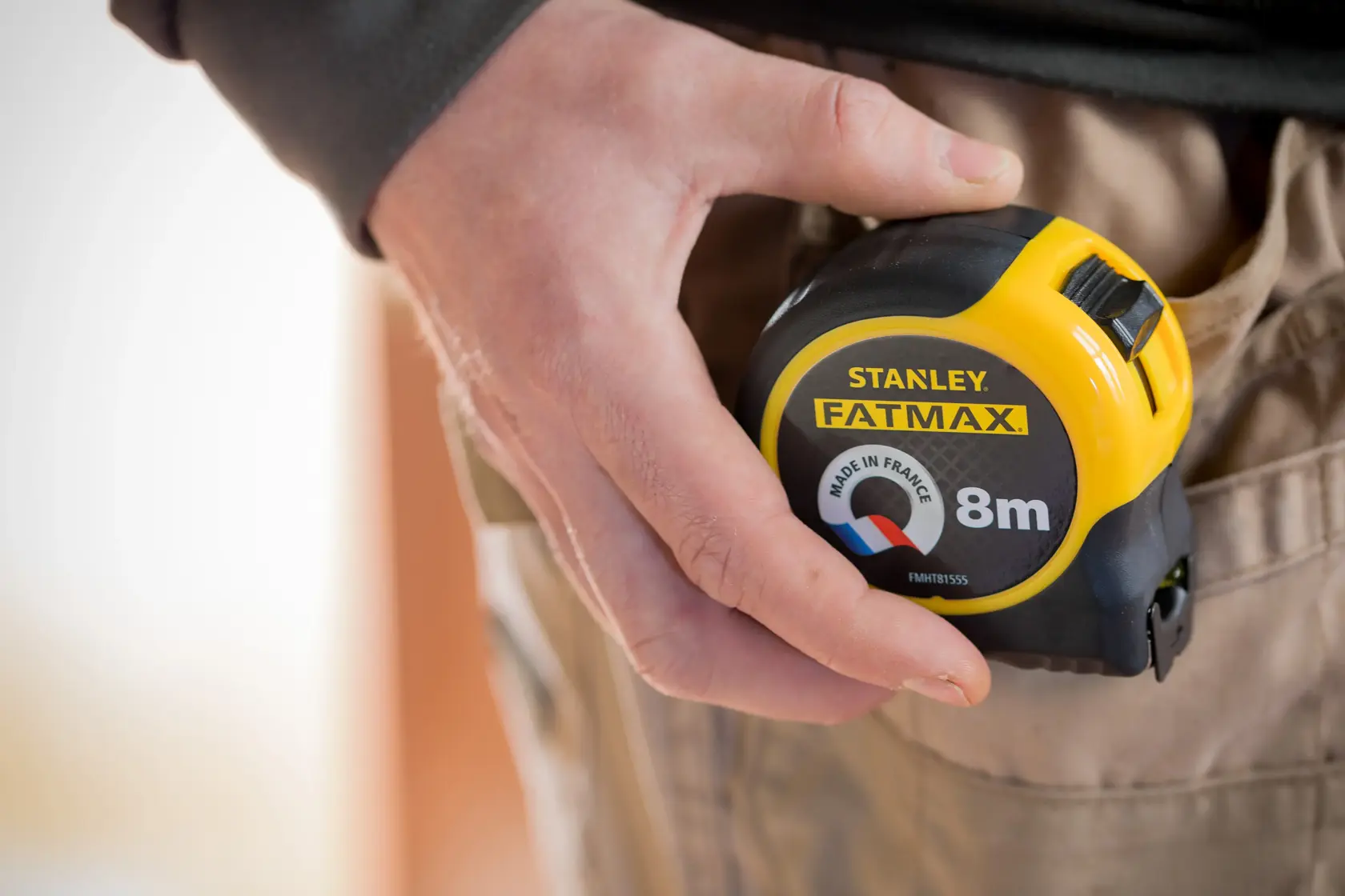 Foto des STANLEY FMHT81555-0 FATMAX 8m Maßbands in der Hand, am beige Arbeitshose befestigt.
