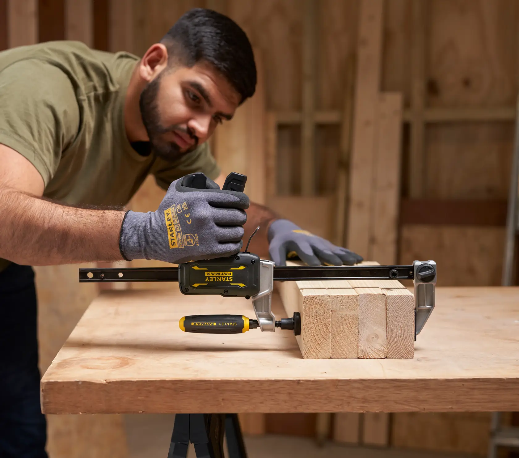 STANLEY FMHT83006-0 Schraubzwinge im Einsatz an Holzbrettern, behandschuhte Hände justieren die Zwinge, Werkstattszene.
