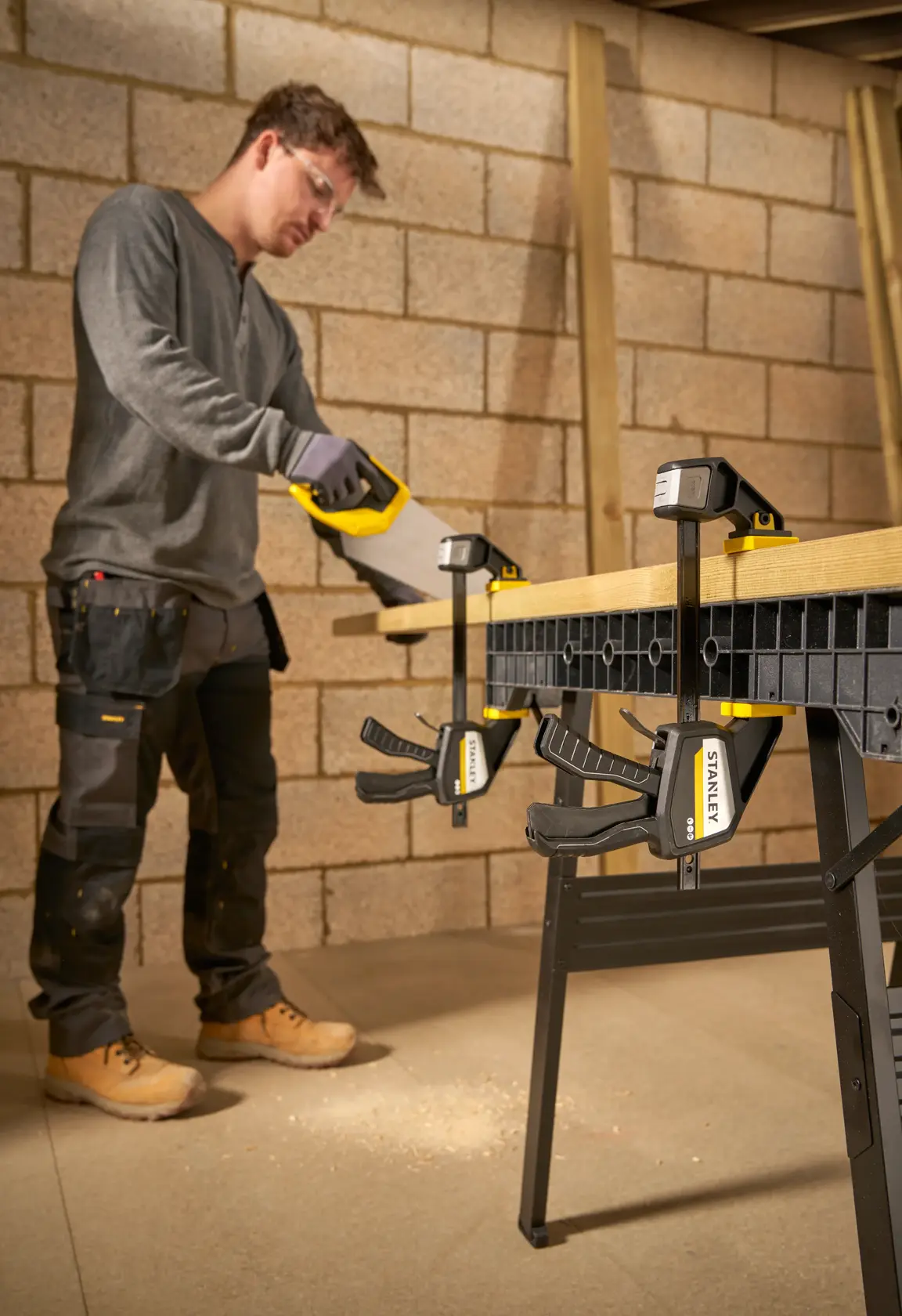 STANLEY FMHT83273-0 Schraubzwinge fixiert Holz an Werkbank, Person sägt in Werkstatt.