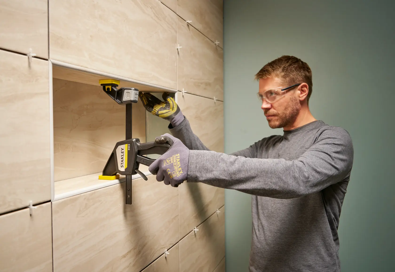 STANLEY FMHT83273-0 Schraubzwinge im Einsatz an gefliester Wand, Person mit Handschuhen hält die Zwinge.