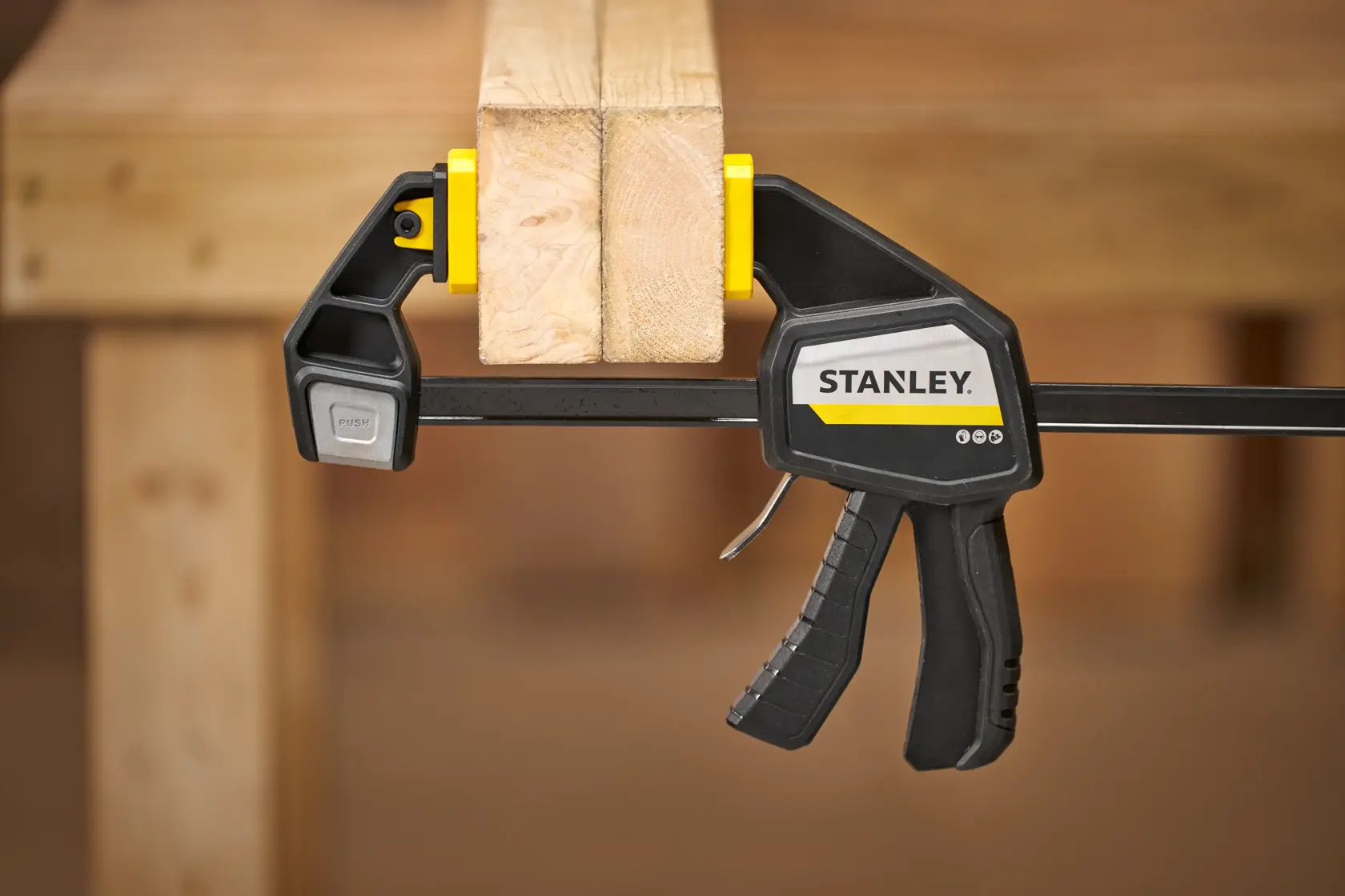 STANLEY FMHT83277-0 Einhandzwinge hält zwei Holzbretter auf einer Werkbank, Seitenansicht.