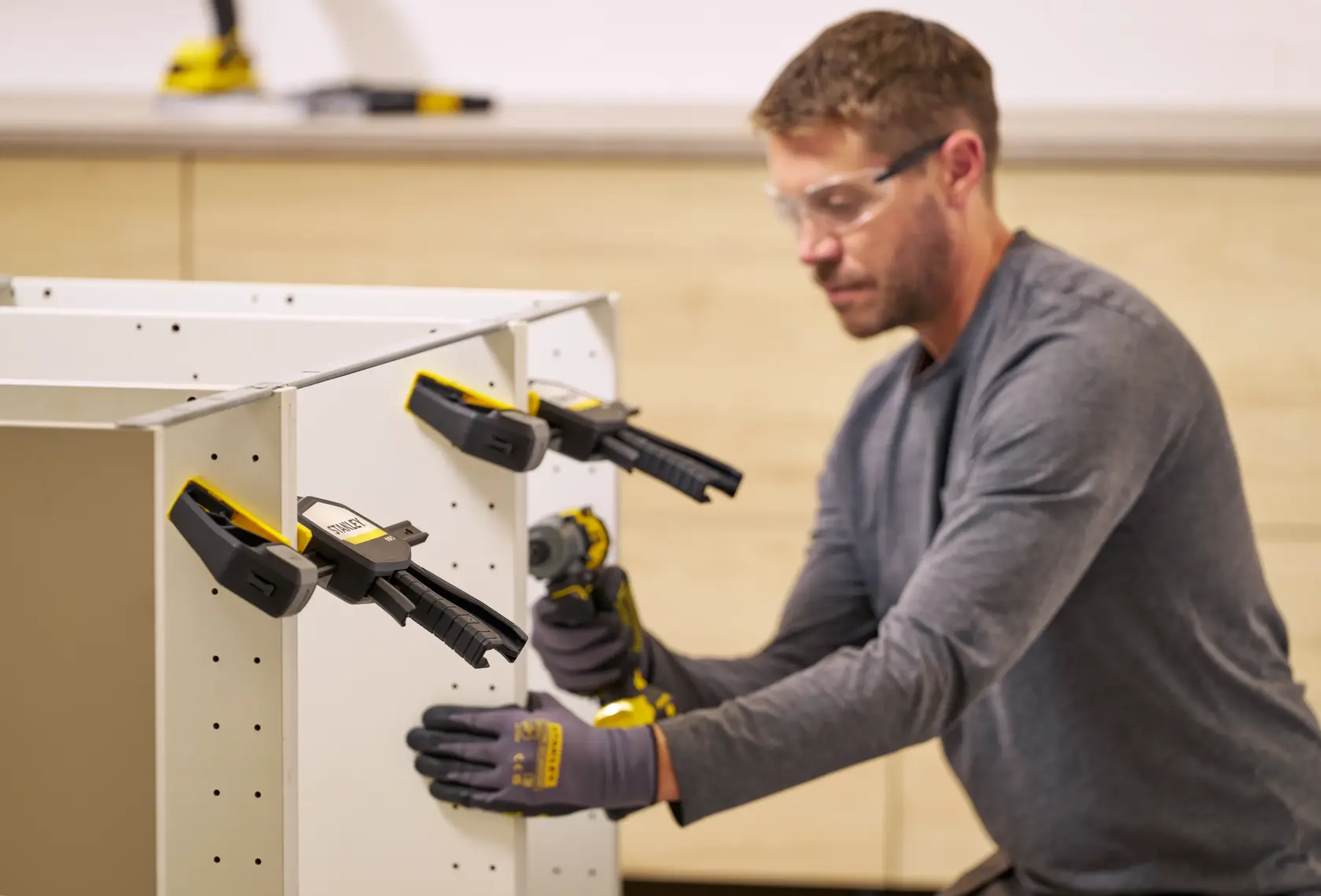 STANLEY FMHT83278-0 Schraubzwingen halten weiße Platten, Person montiert Schrank in Werkstatt.