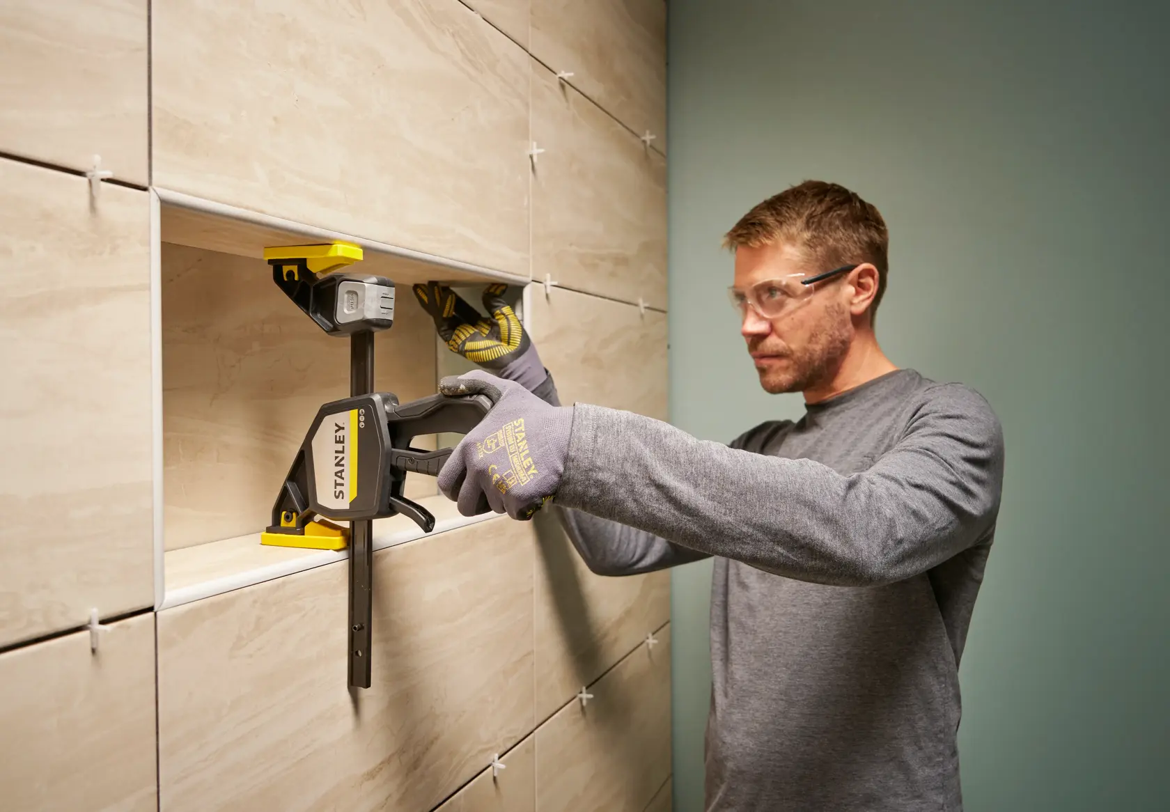 STANLEY FMHT83278-0 Zwinge bei der Fliesenmontage an der Wand, Person mit Handschuhen.