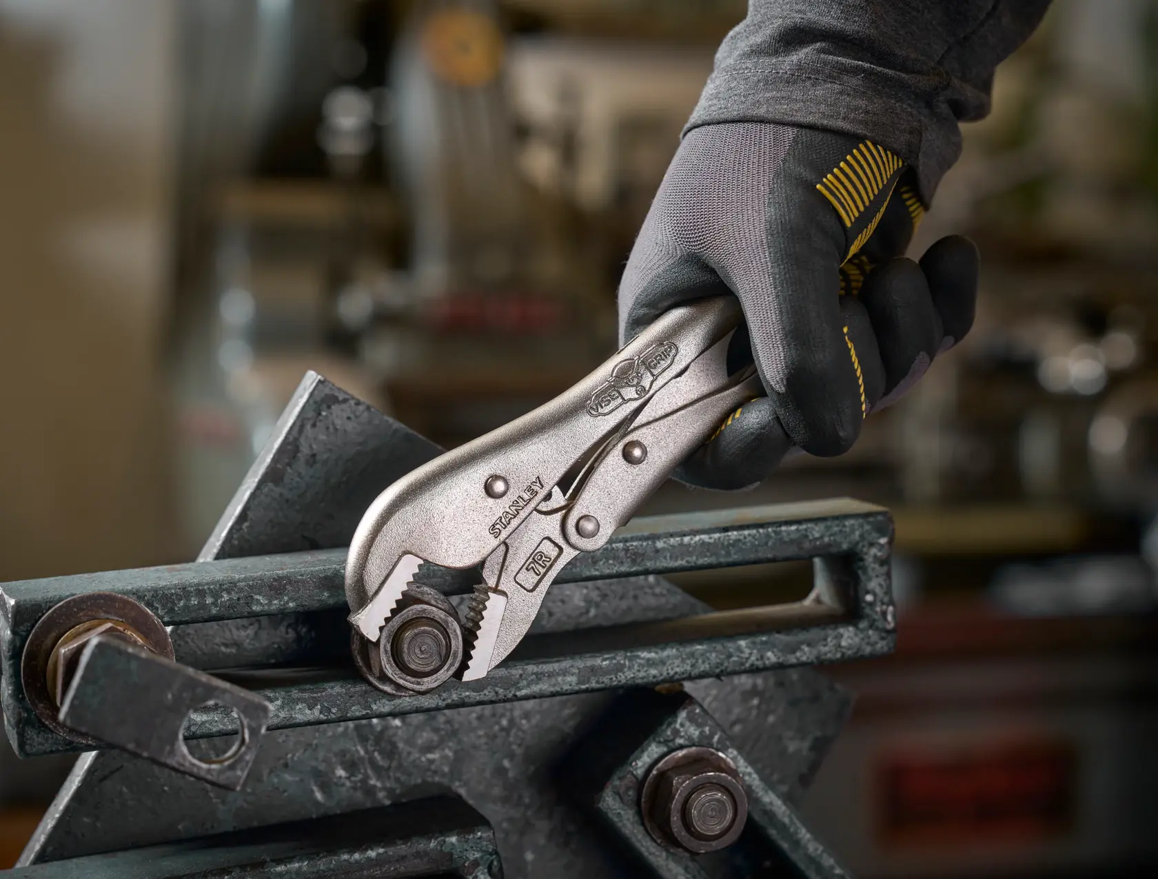 Hand mit Handschuh nutzt STANLEY Gripzange, um eine Metallschraube in der Werkstatt zu halten.