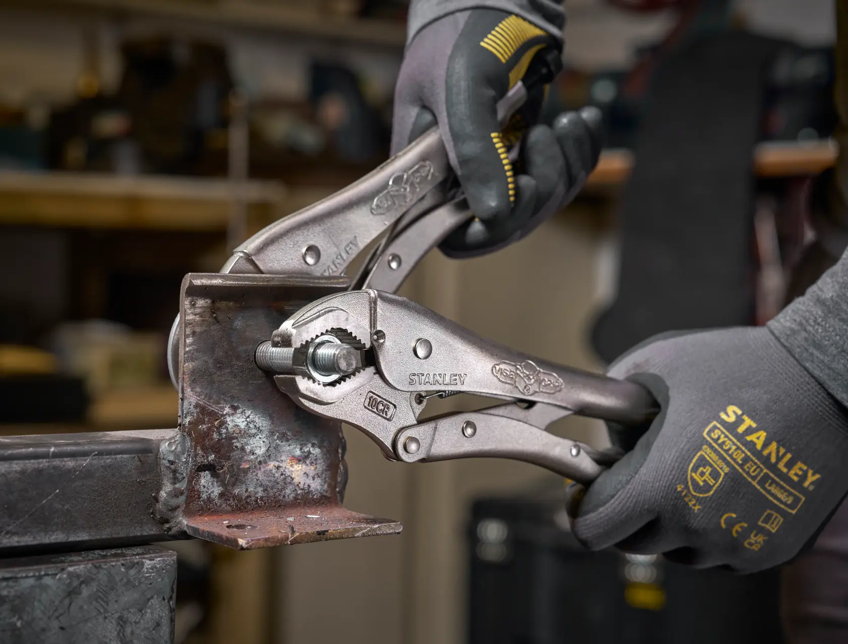 Stanley Klemmzangen greifen Metall, Hände mit Stanley-Handschuhen halten das Werkzeug in einer Werkstatt.