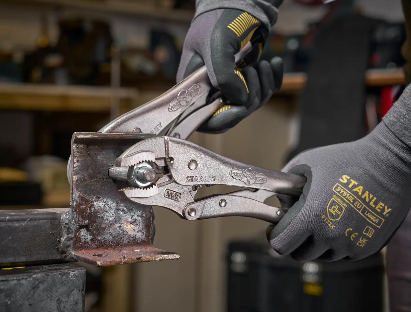 Stanley Feststellzange von Handschuhen gehalten, greift ein Metallstück in einer Werkstatt.