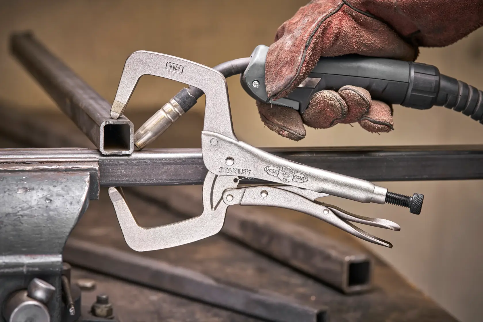STANLEY C-Klemme fixiert Metall beim Schweißen, behandschuhte Hand mit Werkzeug auf Werkbank.