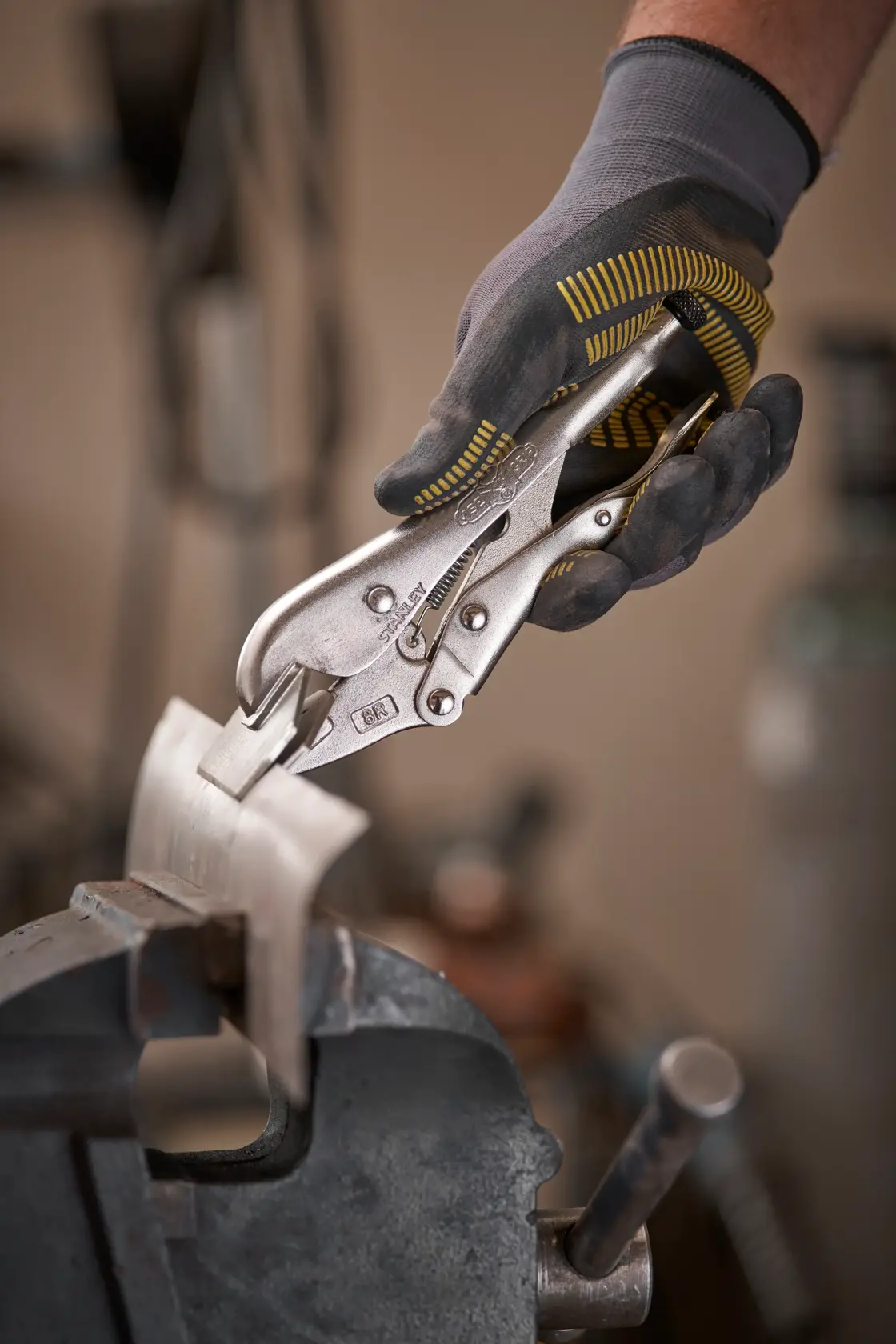 Eine behandschuhte Hand nutzt STANLEY Feststellzange an einem Metallteil im Schraubstock.