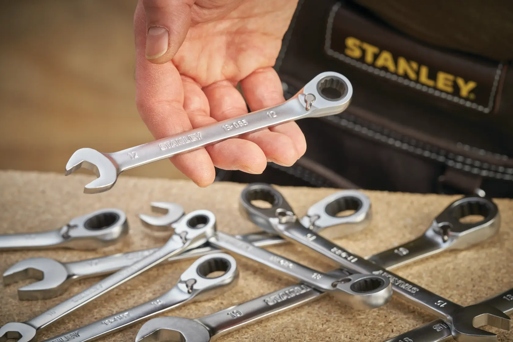 Photo of STANLEY FMMT13087-0 wrench set, silver wrenches on table, one held in hand, close-up angle.