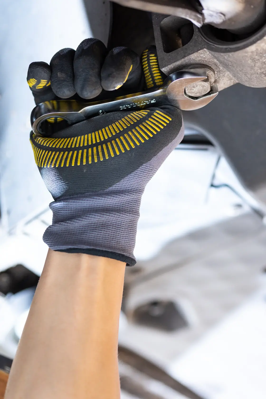 STANLEY FMMT13098-0 mechanics glove with yellow grip detail holding wrench, close-up during automotive repair.