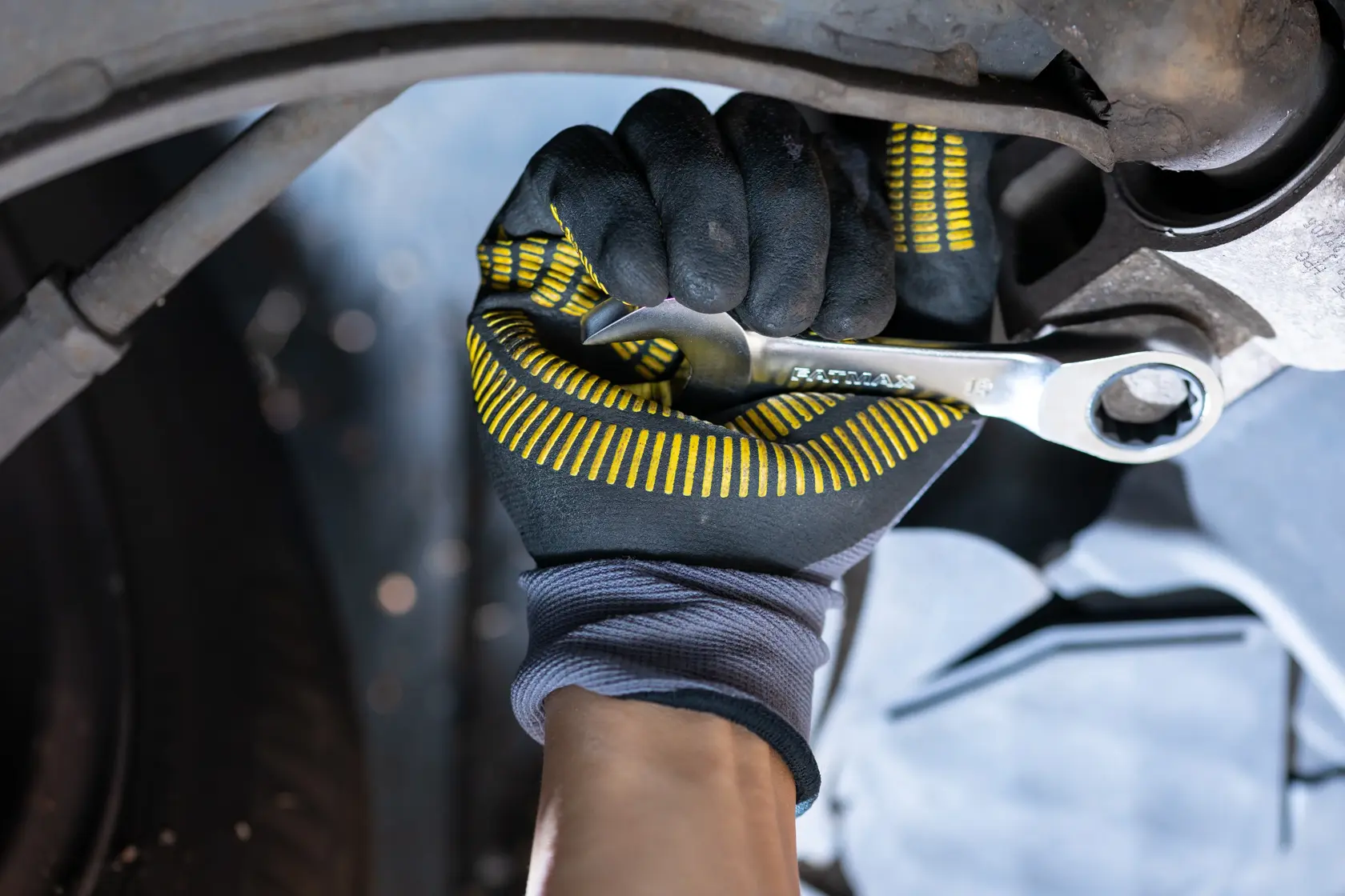 STANLEY FMMT13112-0 wrench in gloved hand tightening bolt, close-up of tool in automotive repair context.