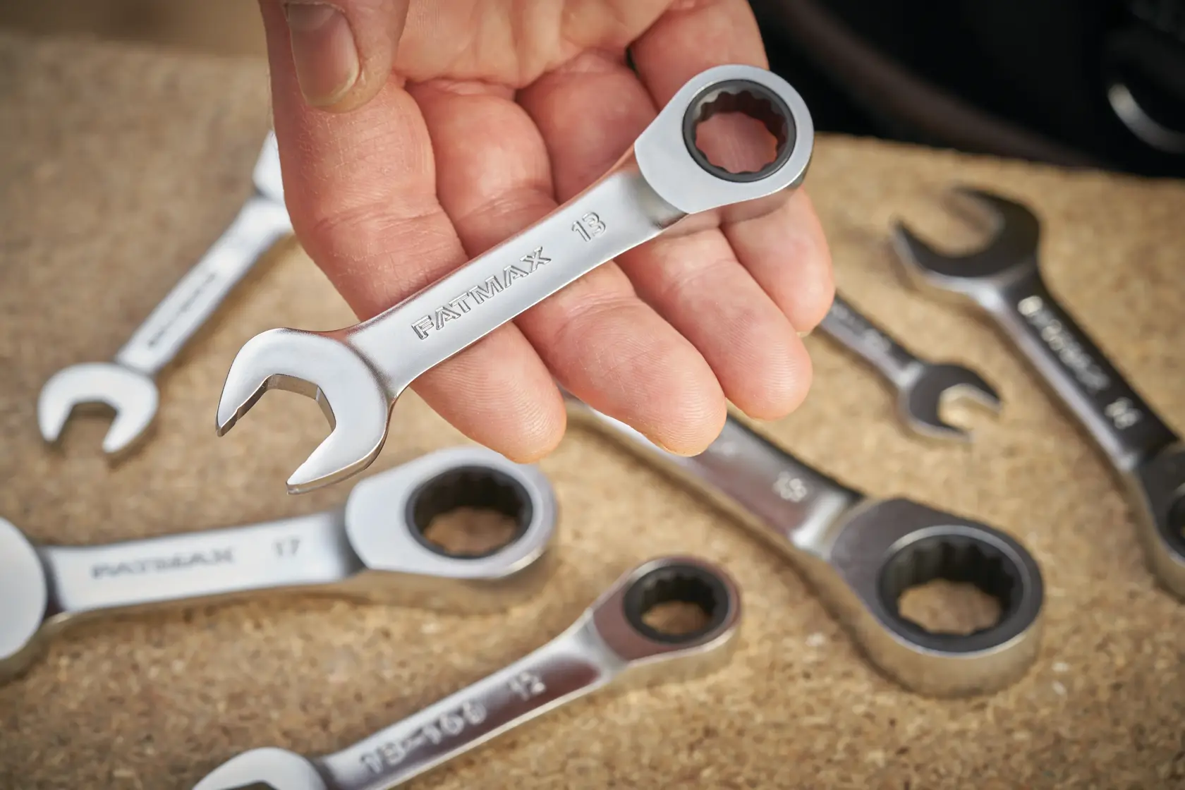 Photo of STANLEY FMMT13113-0 ratcheting combination wrenches, one held in hand, others on work surface.