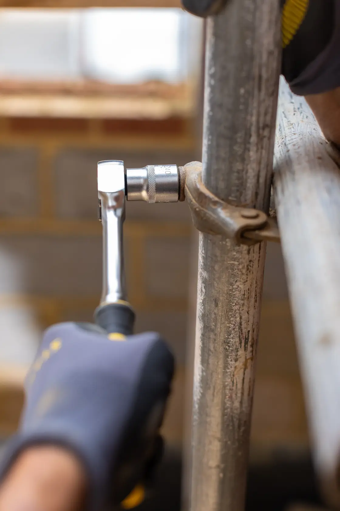 STANLEY FMMT17220-0 ratchet wrench in use on scaffolding pipe, close-up, user wearing work gloves.