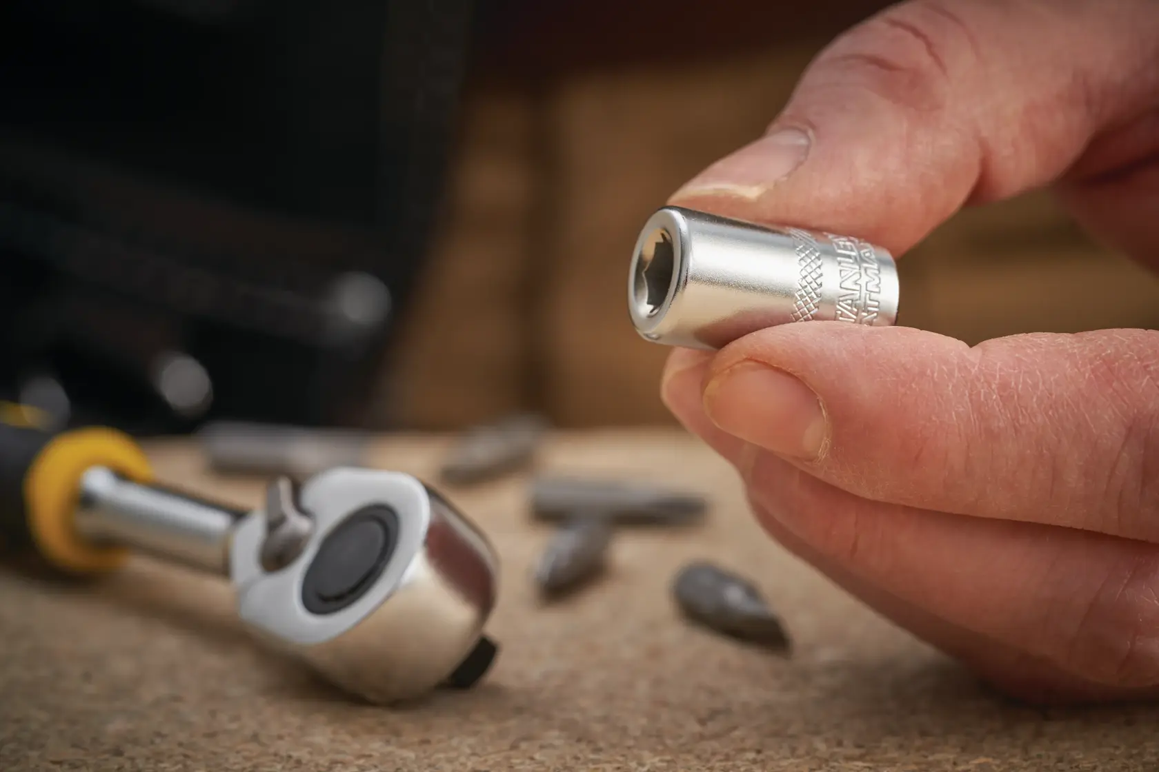 STANLEY FMMT18007-0 Steckschlüssel in der Hand, Ratsche und Bits auf Tisch, Nahaufnahme.