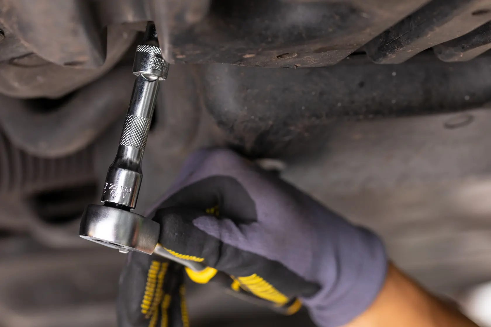 STANLEY FMMT25123-0 ratchet wrench used on bolt, close-up, automotive repair, gloved hand.