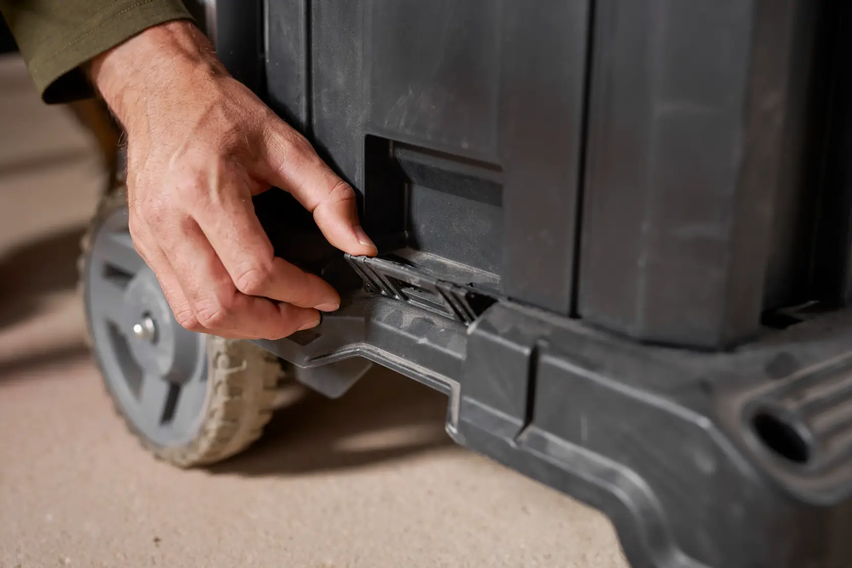 STANLEY FMST1-72363 tool box close-up showing hand opening the latch near wheel, photography.