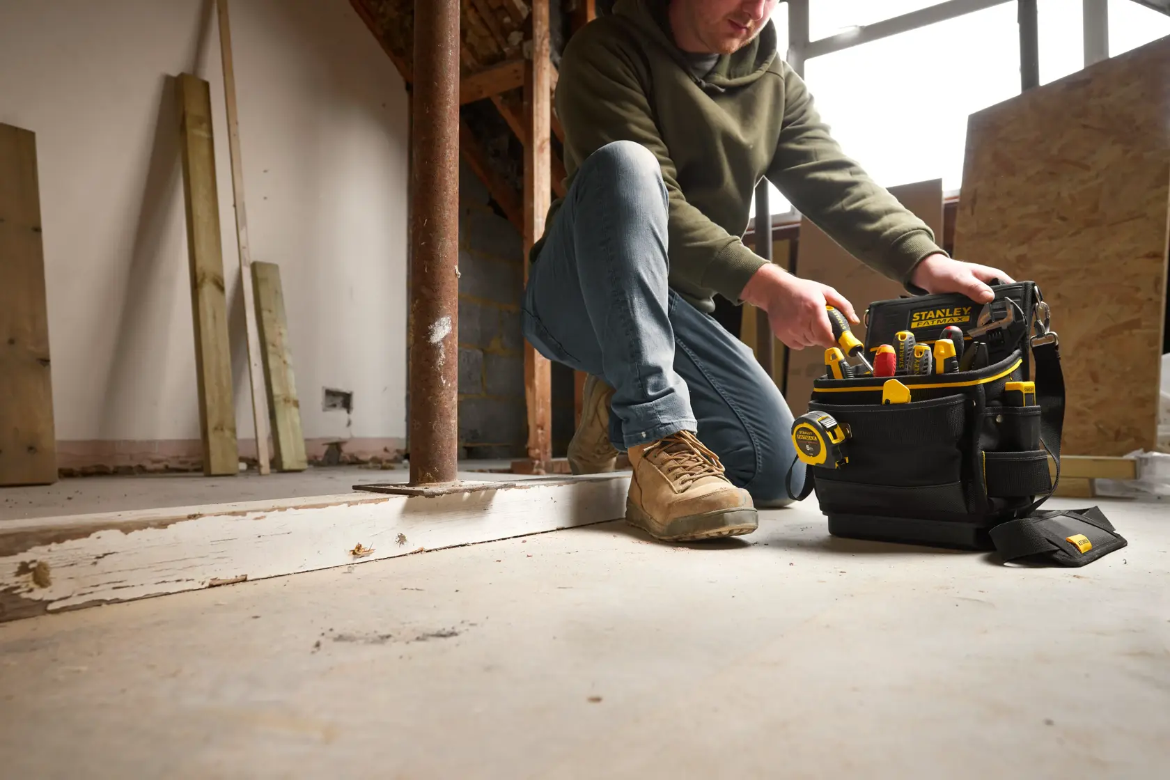 Stanley FMST17624-1 tool bag with yellow tools on construction site, person kneeling beside bag.