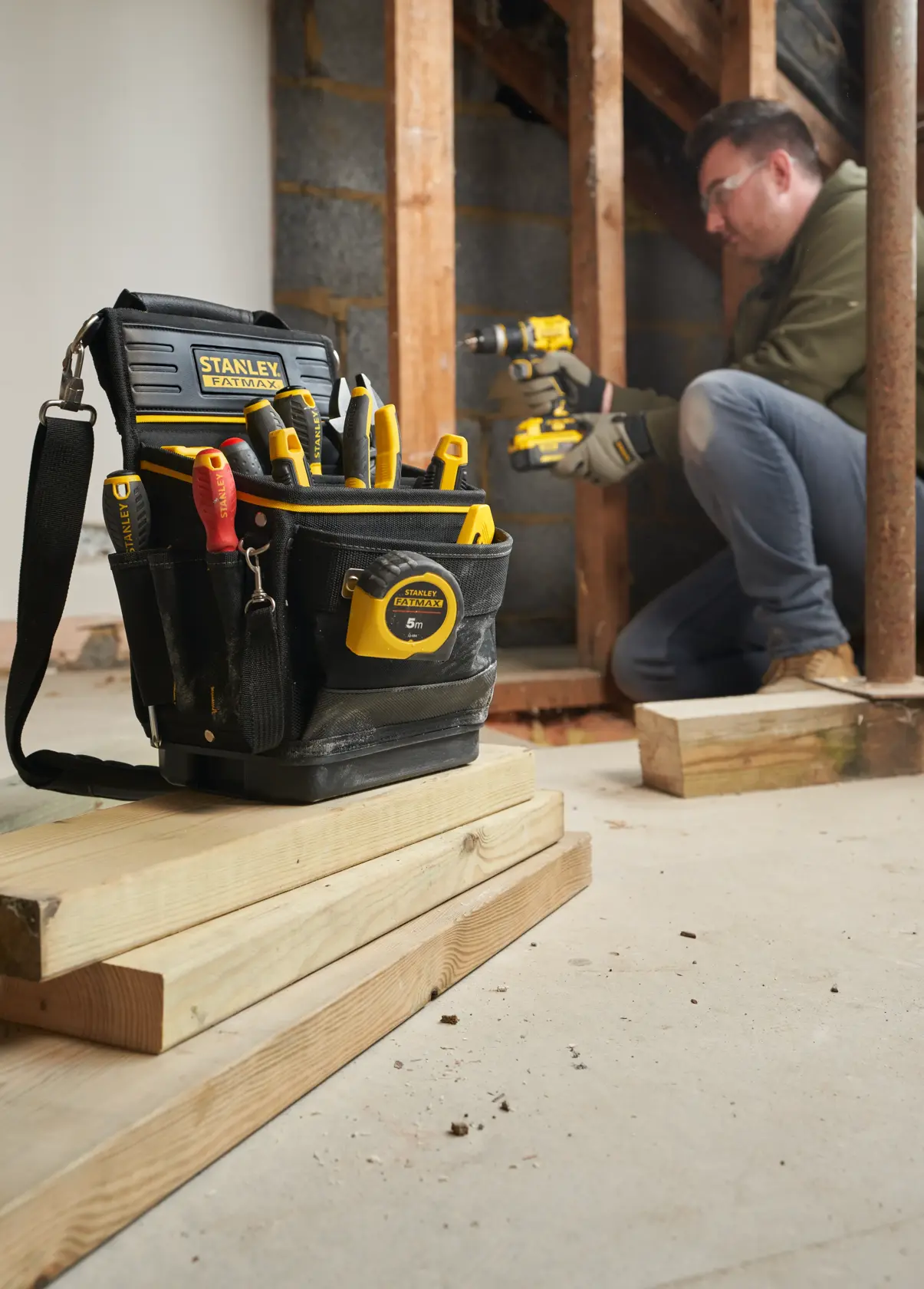 STANLEY FMST17624-1 tool bag filled with hand tools, tape measure, and drill, shown at a construction site.