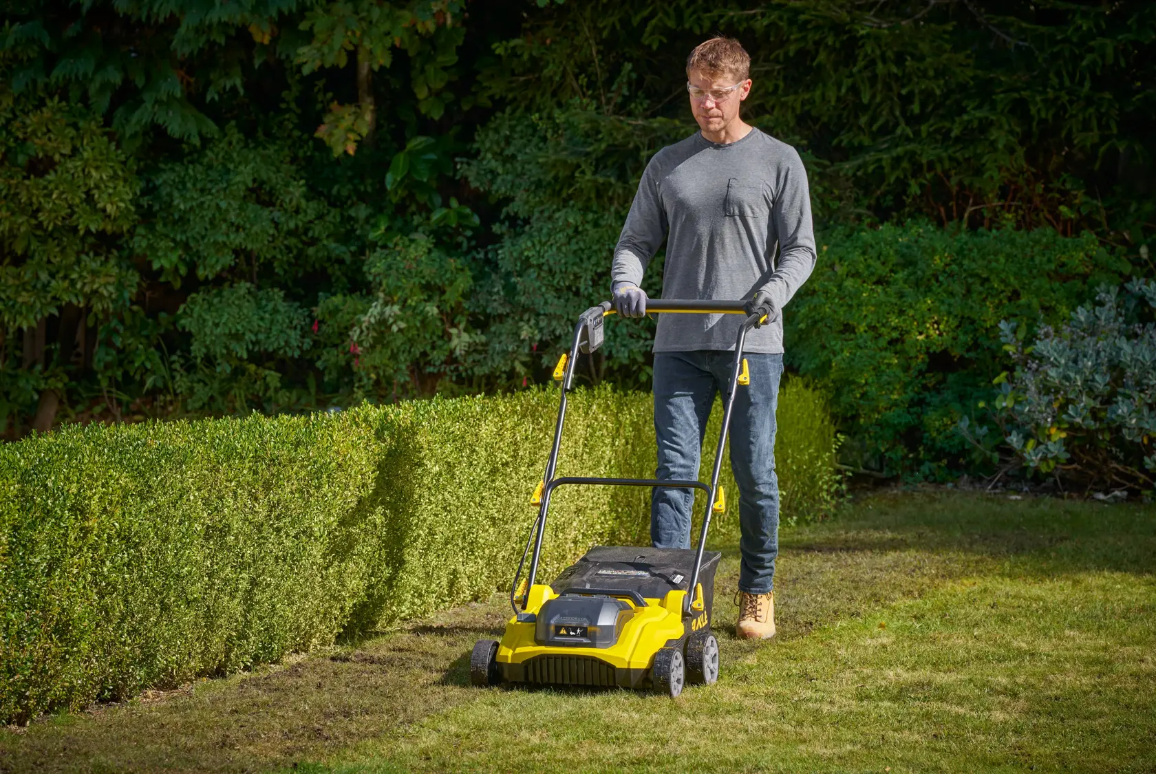 Foto des STANLEY SCOEP3801M2 Rasenvertikutierers im Einsatz auf einer Gartenrasenfläche, bedient von einer Person im Freien.