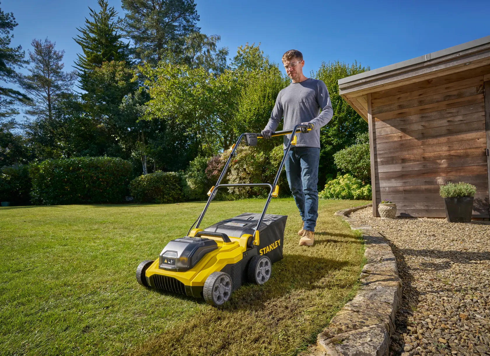 STANLEY SCOEP3801N Vertikutierer im Einsatz auf dem Gartenrasen, Außenansicht mit Gartenhaus.
