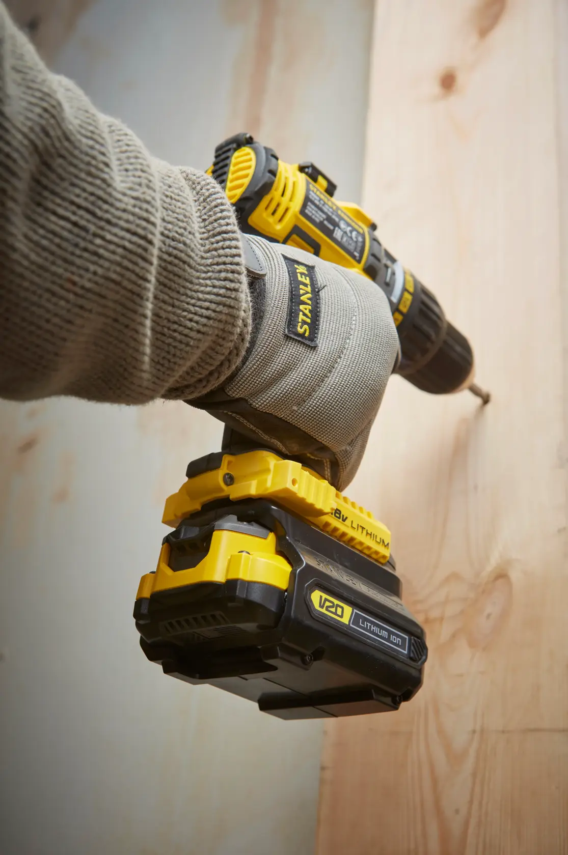 STANLEY SFMCB121D1 cordless drill in use, yellow and black, shown close-up during wood drilling.