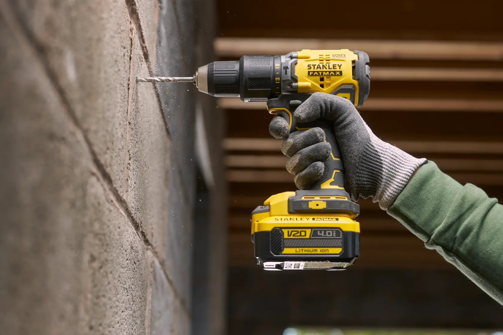 STANLEY SFMCB14M1 Akku-Bohrmaschine im Einsatz, bohrt in Betonwand, Nahaufnahme von Werkzeug und behandschuhter Hand.