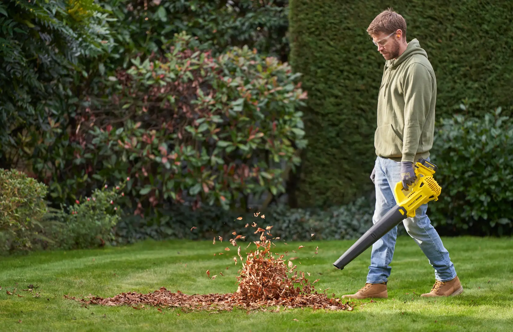 STANLEY SFMCBL714B-XJ Laubbläser im Einsatz auf Rasen, bläst einen Haufen trockener Blätter im Garten.